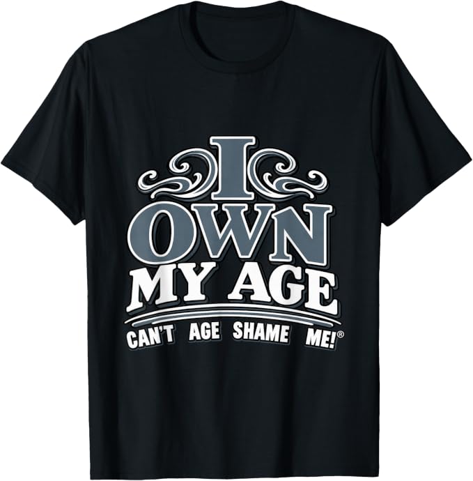 Black T-shirt with gray and white lettering reading “I Own My Age” and “Can’t Age Shame Me!®,” with decorative flourishes.