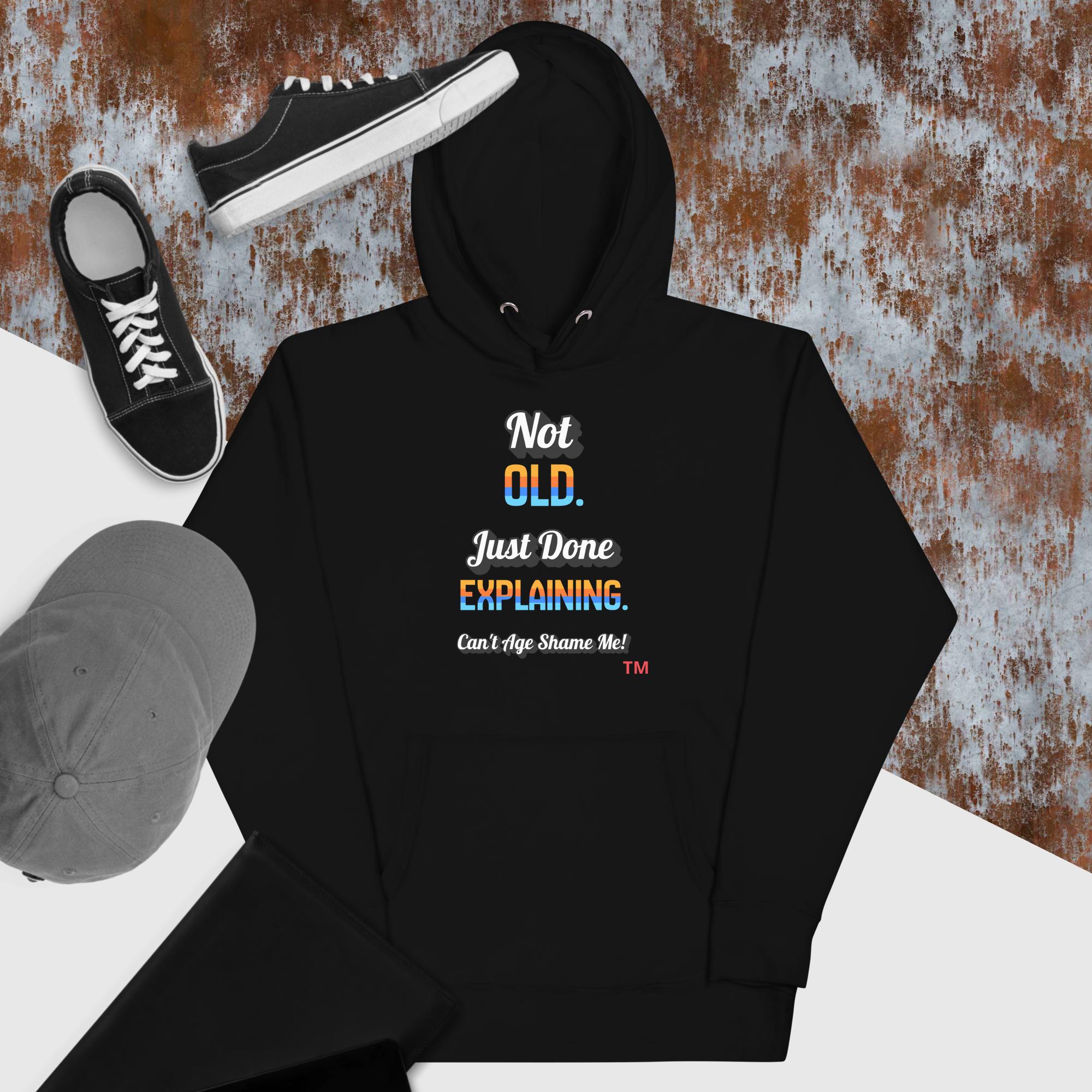 Black hoodie with humorous text design, paired with black sneakers and a gray cap on a textured surface.