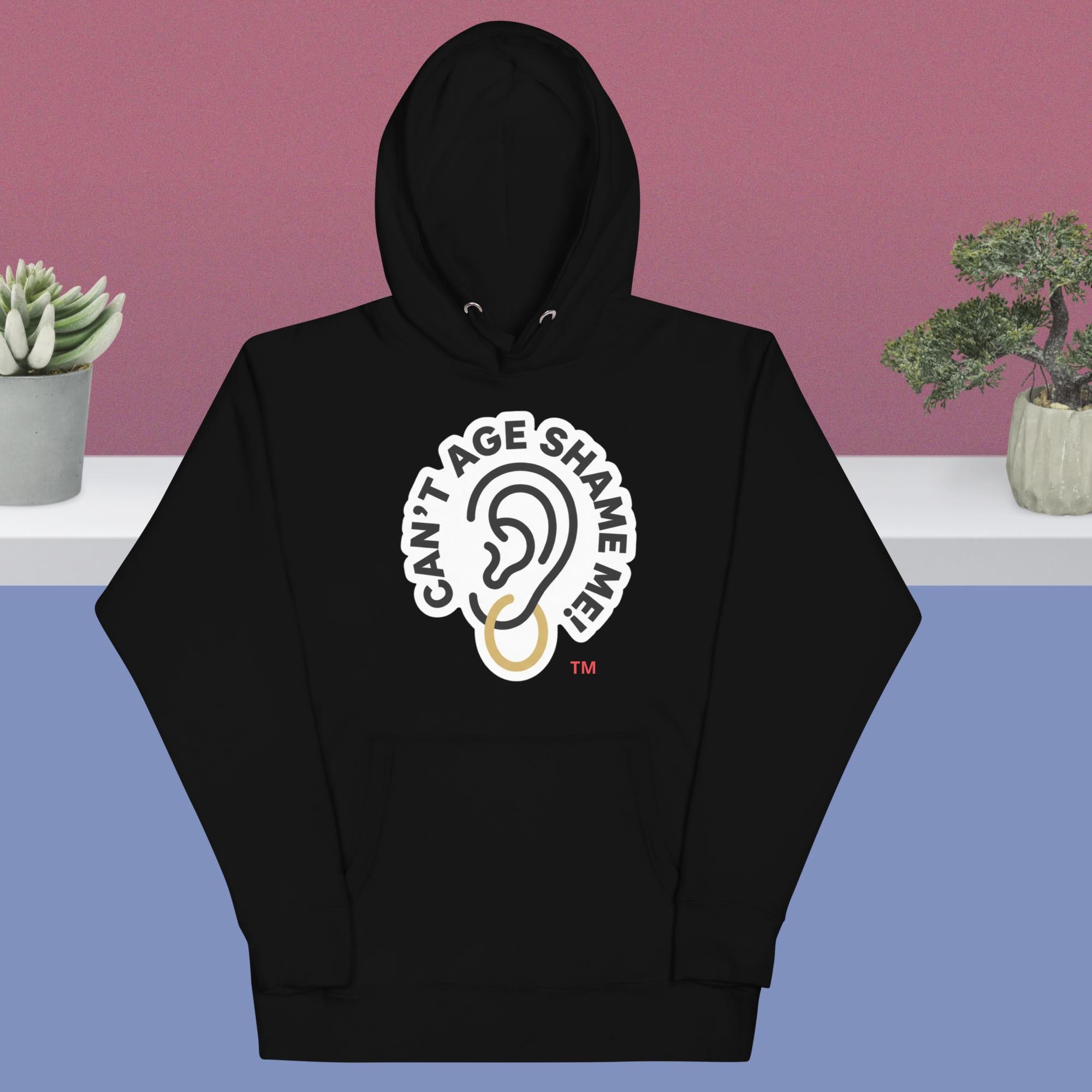 Black hoodie with 'Can't Age Shame Me' design on a blue and pink gradient background