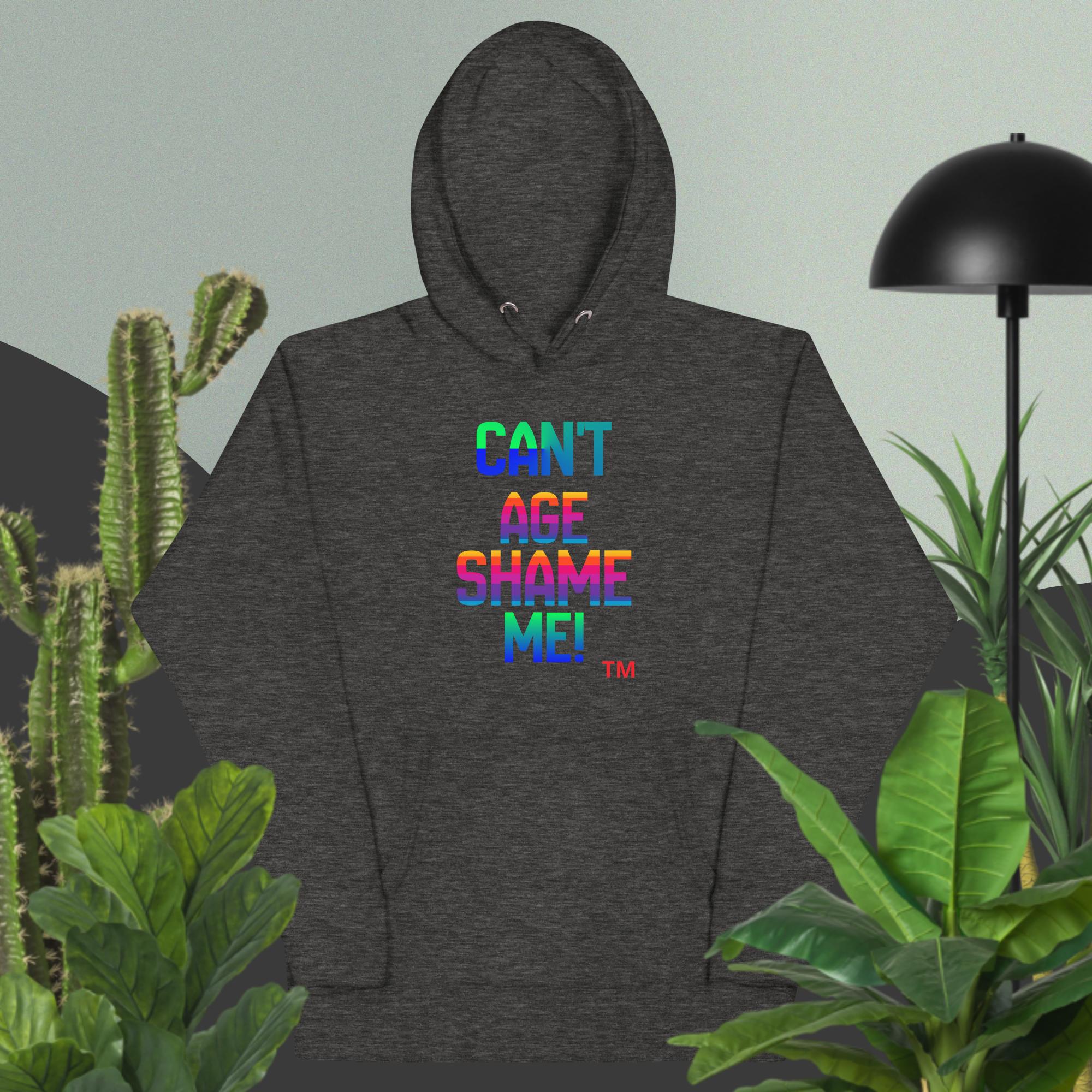 Dark gray hoodie with colorful text 'CAN'T AGE SHAME ME!' on a light green background with plants.