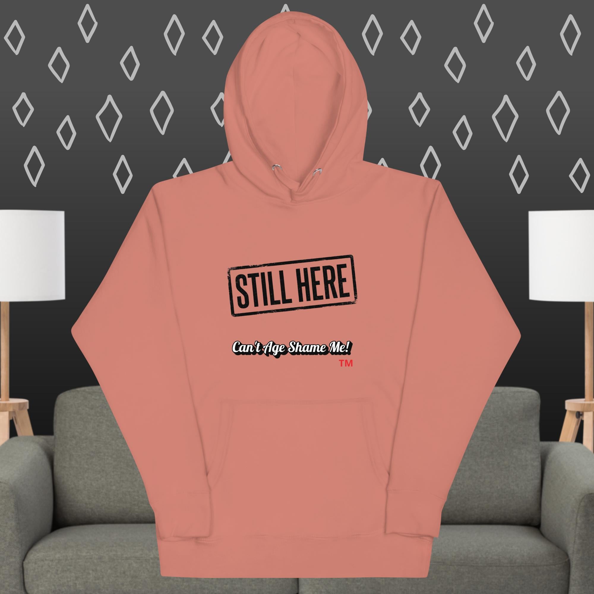 Dusty Rose hoodie with text design on a gray couch against a dark wall with diamond pattern
