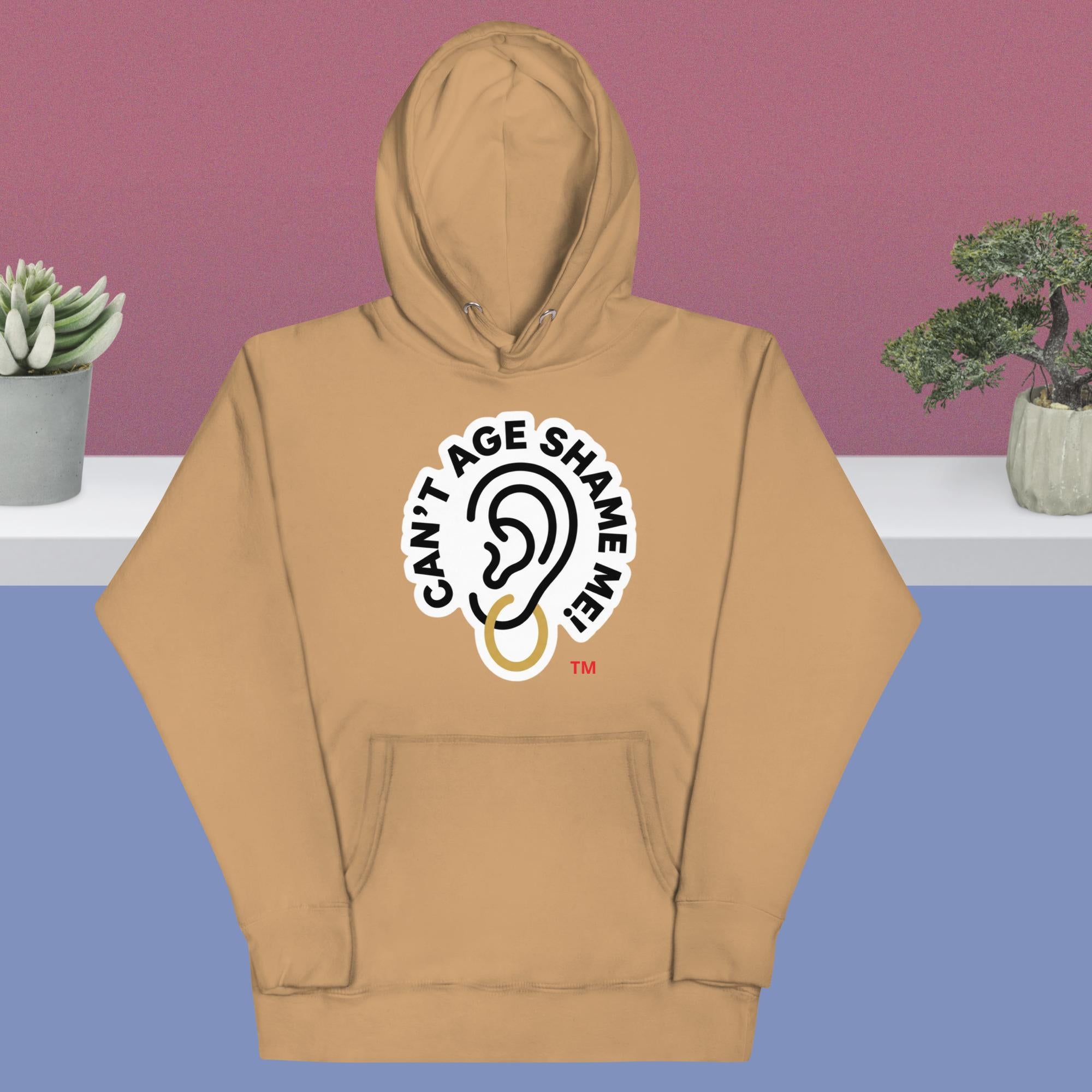 Khaki hoodie with 'Can't Age Shame Me!' logo on a purple and blue gradient background