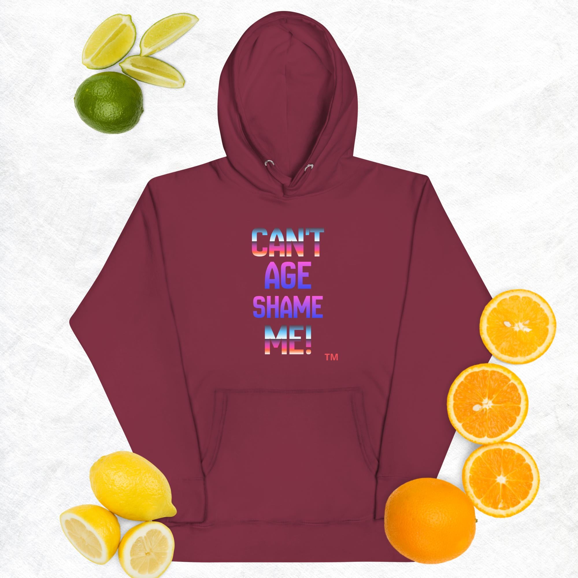 Maroon hoodie with 'CAN'T AGE SHAME ME!' text, surrounded by fruits on a light background