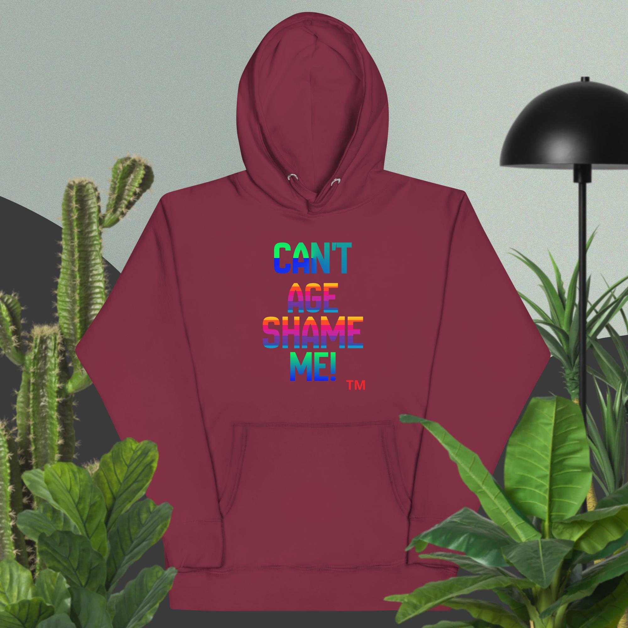 Maroon hoodie with colorful text design in a room with plants and a lamp.