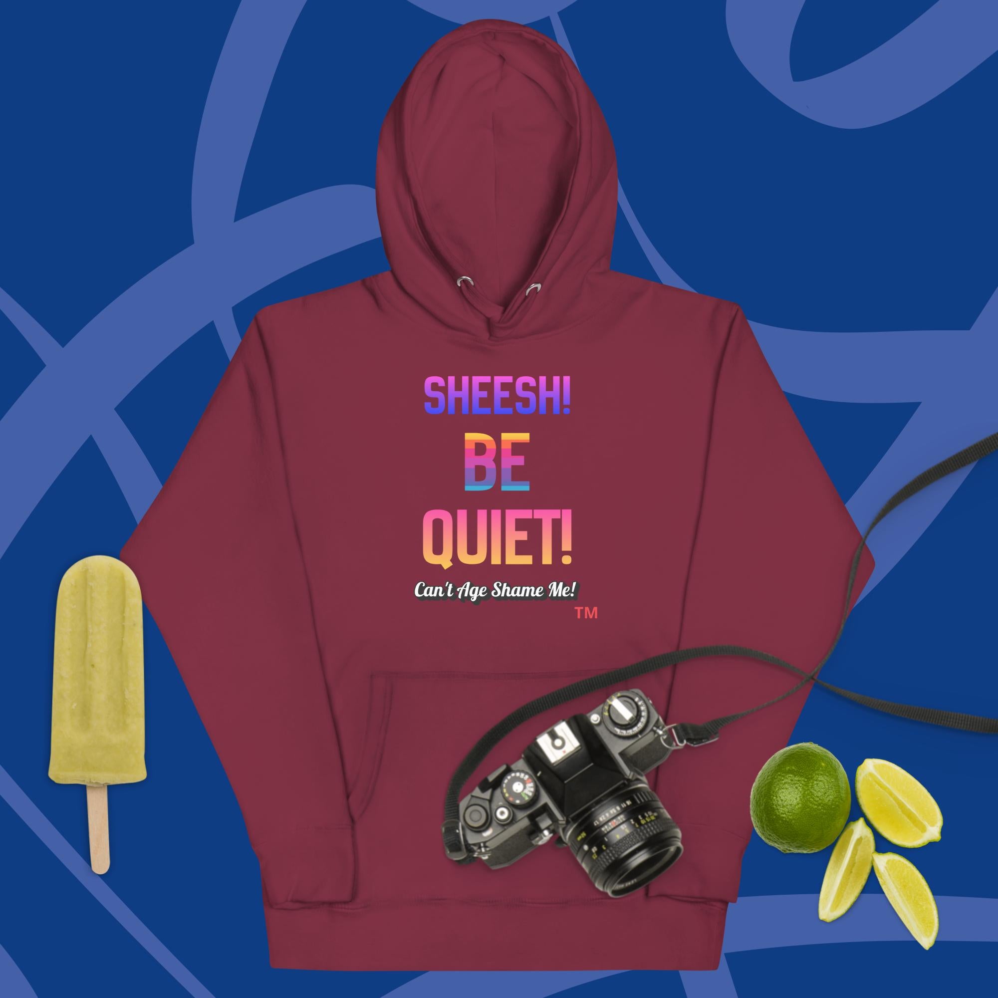 Maroon hoodie with colorful text: Sheesh! Be Quiet! 'Can't Age Shame Me!
 on a blue background with camera, popsicle, and limes.


