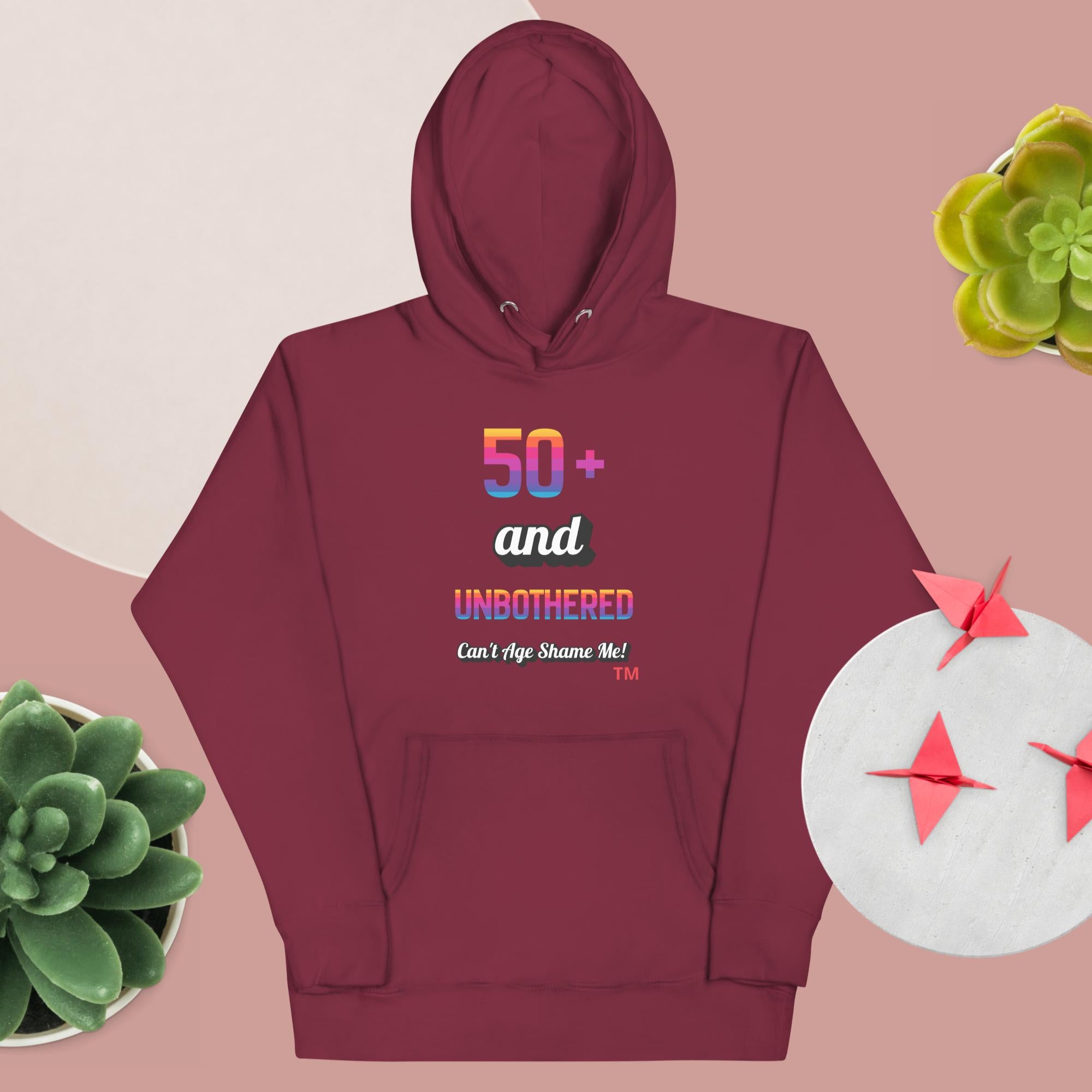 Maroon hoodie with colorful text design on a pink background with decorative elements.