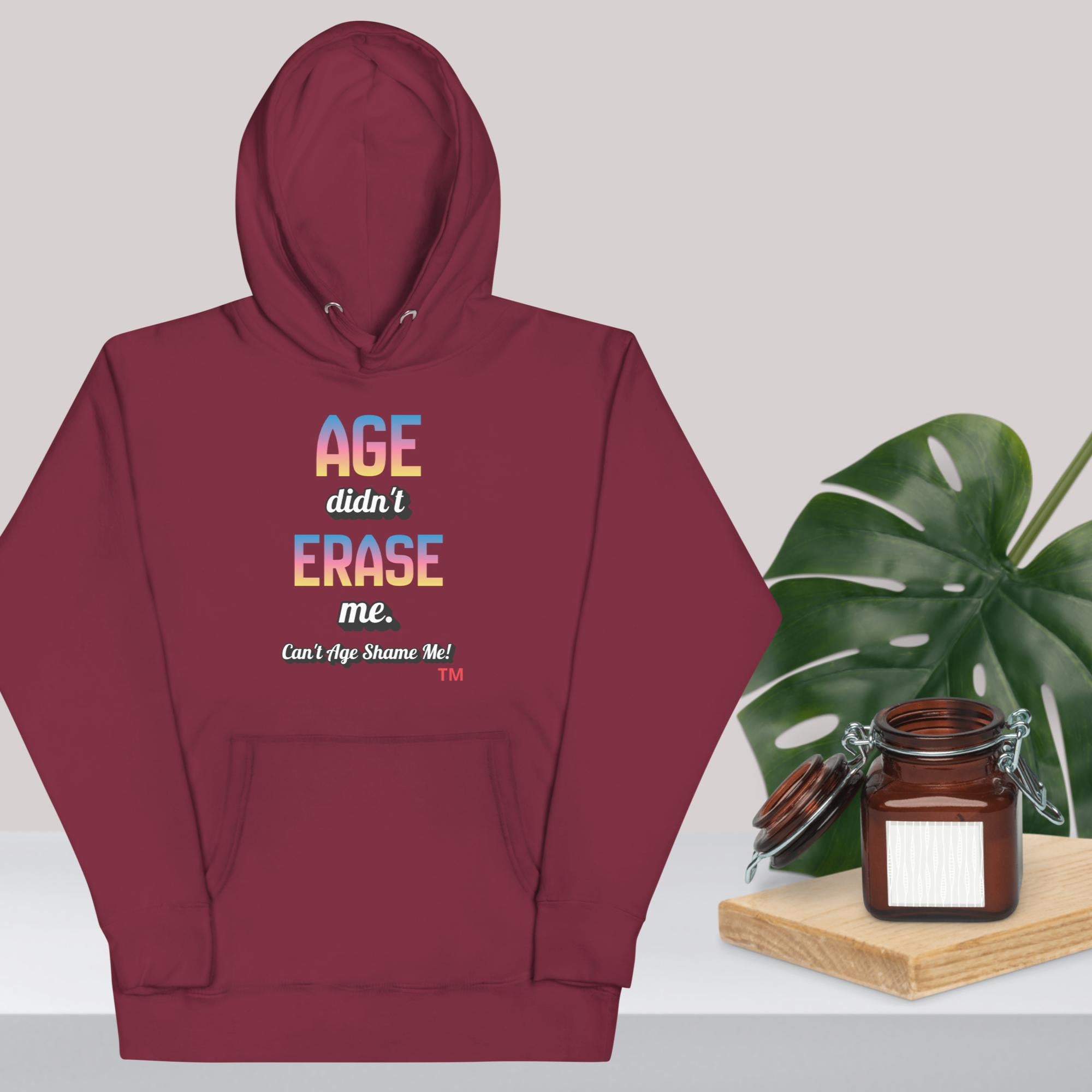 Maroon hoodie with colorful text design on a light gray background with a plant and jar.