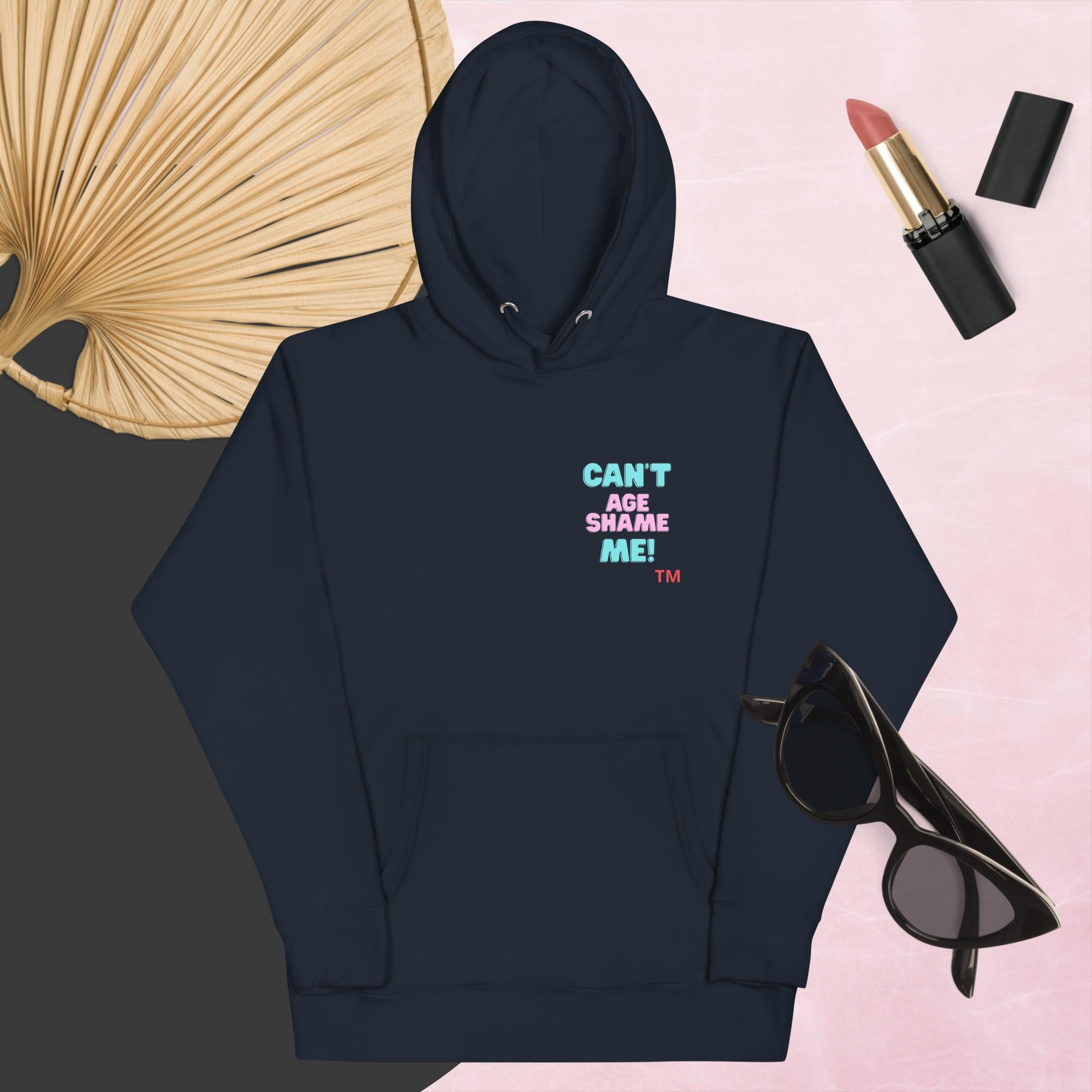 Navy Blazer hoodie with text, 'Can't Age Shame Me' with sunglasses, lipstick, and a decorative leaf on a pink background