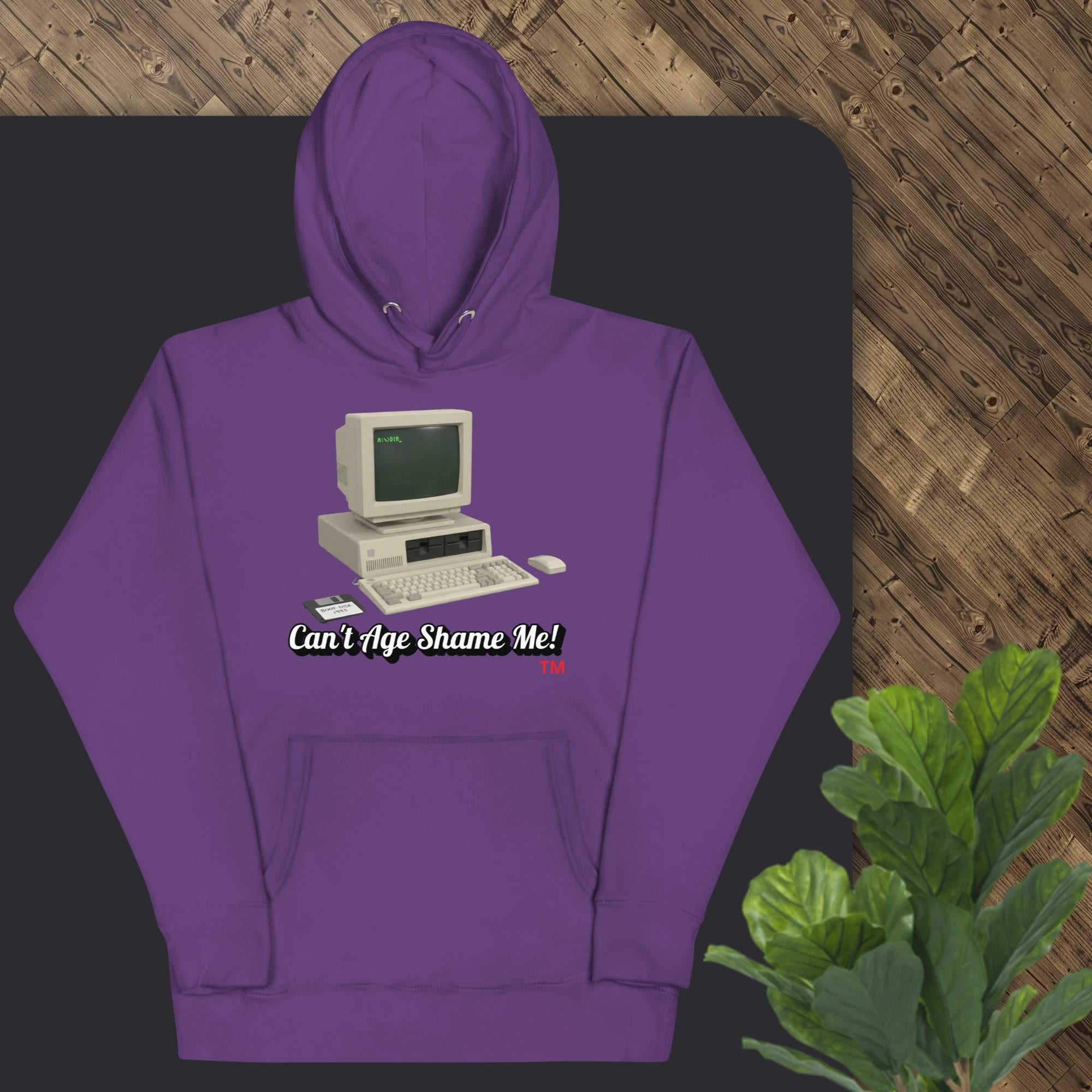 Purple hoodie with vintage computer graphic and text 'Can't Age Shame Me!' on a dark surface.