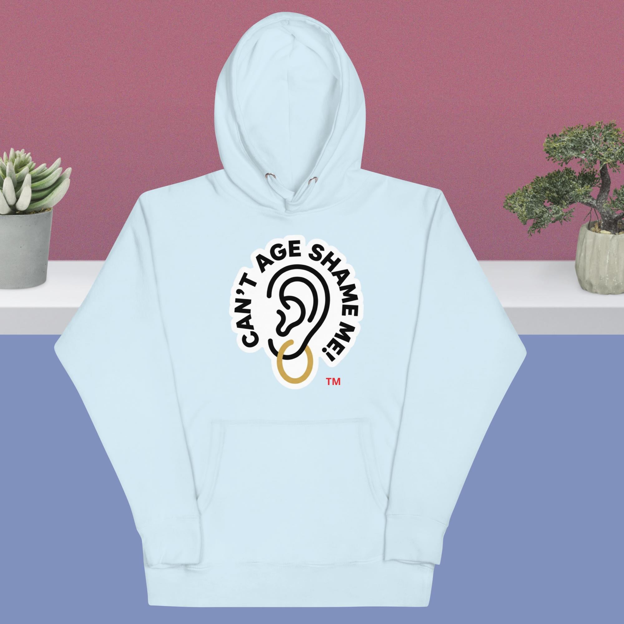 Sky blue hoodie with 'Can't Age Shame Me' logo on a pink and blue gradient background.