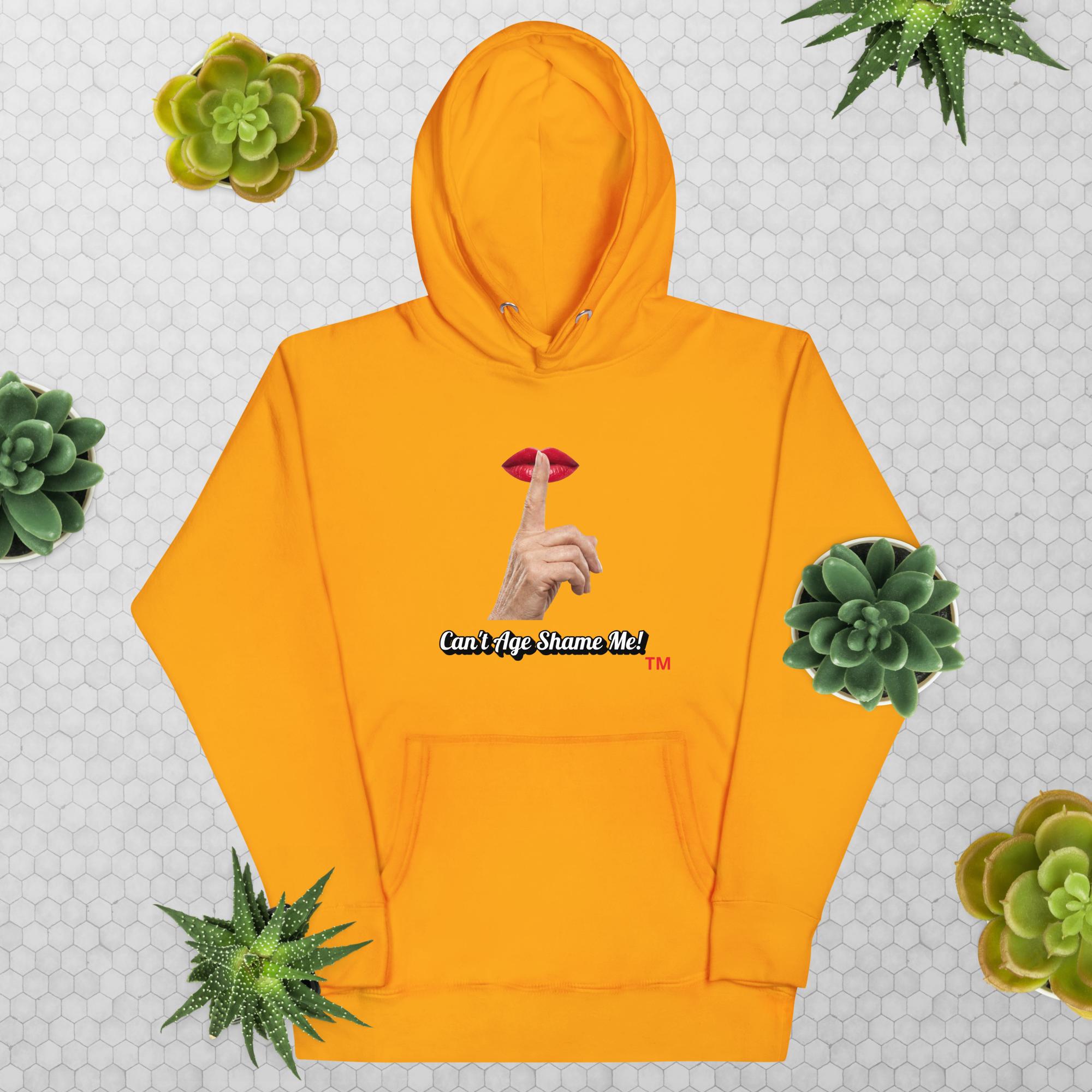 Team Gold hoodie with graphic design and text, Can’t Age Shame Me!, on a patterned background with succulents