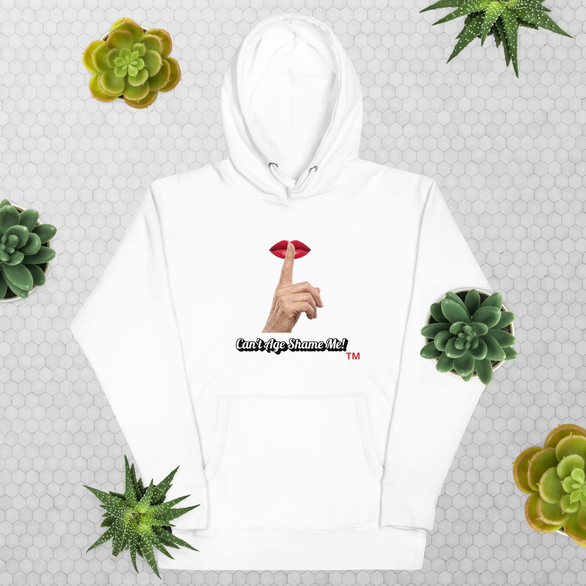 White blue hoodie with graphic design and text, Can’t Age Shame Me!, on a patterned background with succulents
