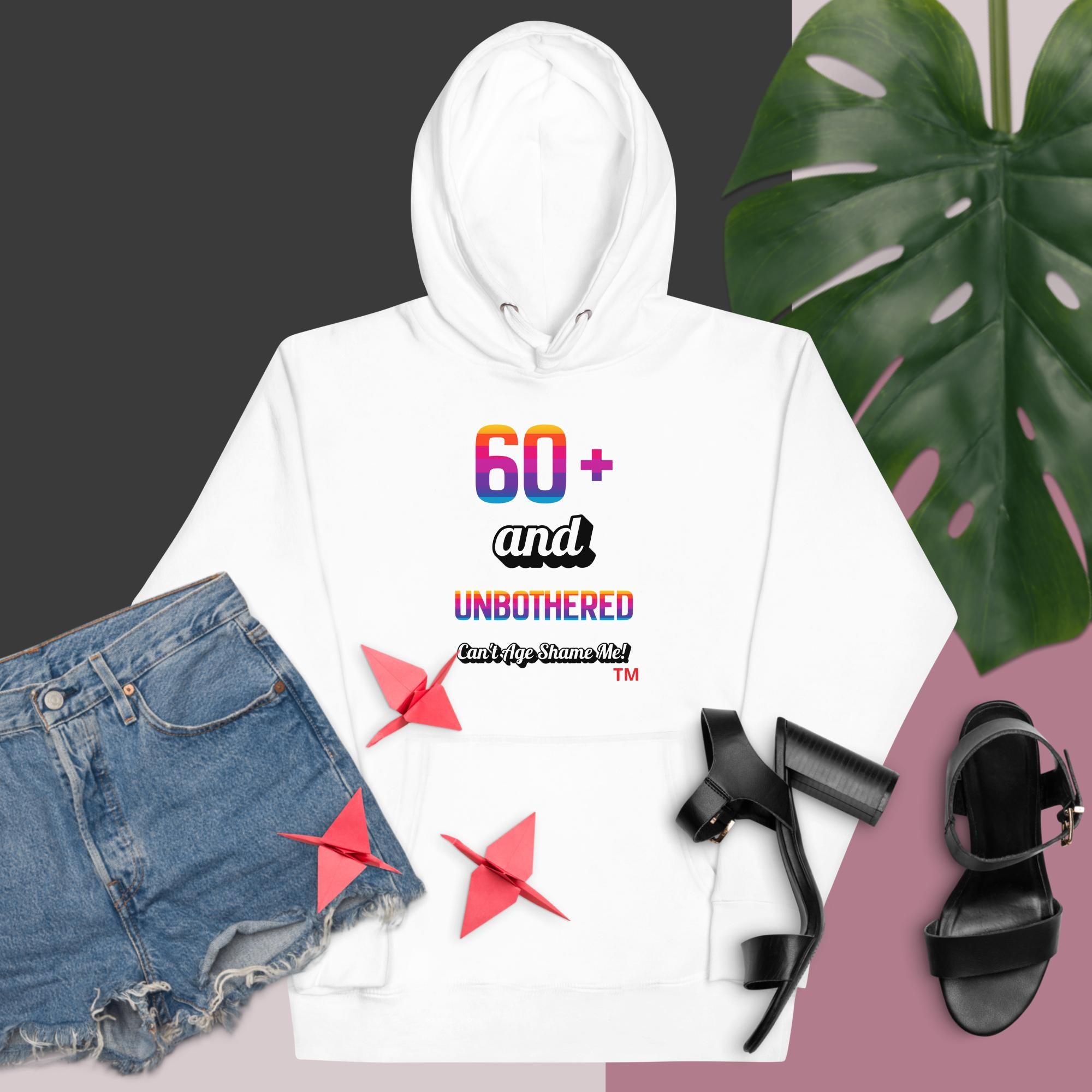 White hoodie with colorful text, denim shorts, black sandals, and a monstera leaf on a gradient background