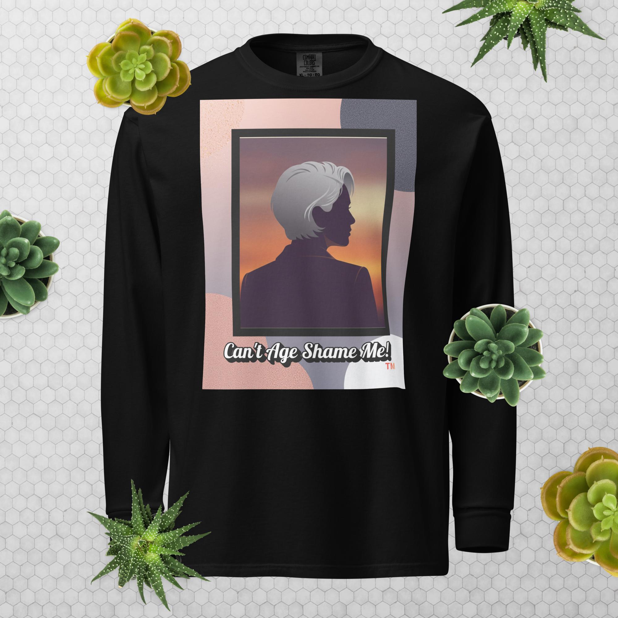 Black long-sleeve shirt with a graphic design featuring a woman with gray hair silhouette and text: Can’t Age Shame Me! surrounded by decorative plants on a light gray background.


