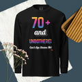 Black long-sleeve shirt with colorful text design on a textured surface with flowers and wooden object.
