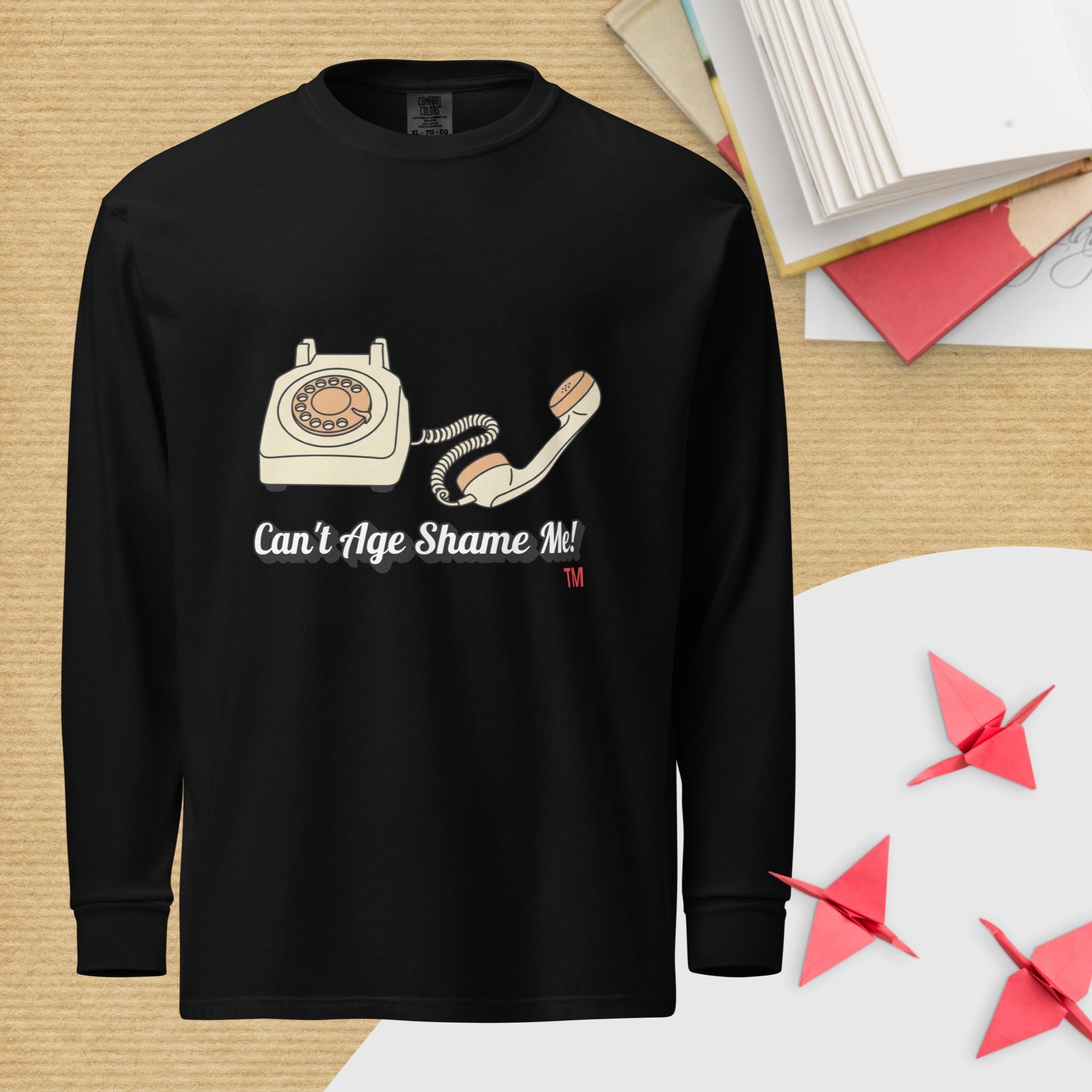 Black long-sleeve shirt with a graphic of an old telephone and text 'Can't Age Shame Me!' on a wooden surface.
