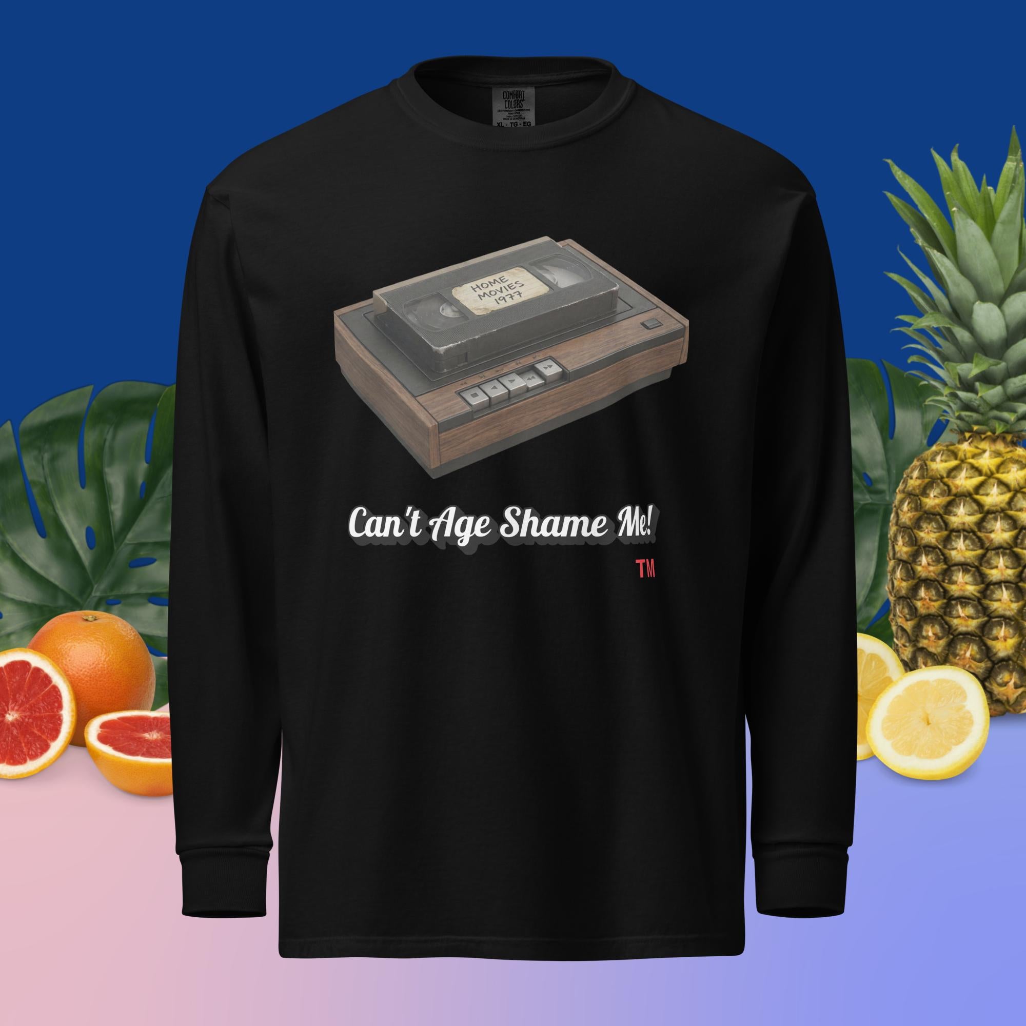 black long-sleeve shirt with a VHS tape design and text can't age shame me, surrounded by fruits and plants.