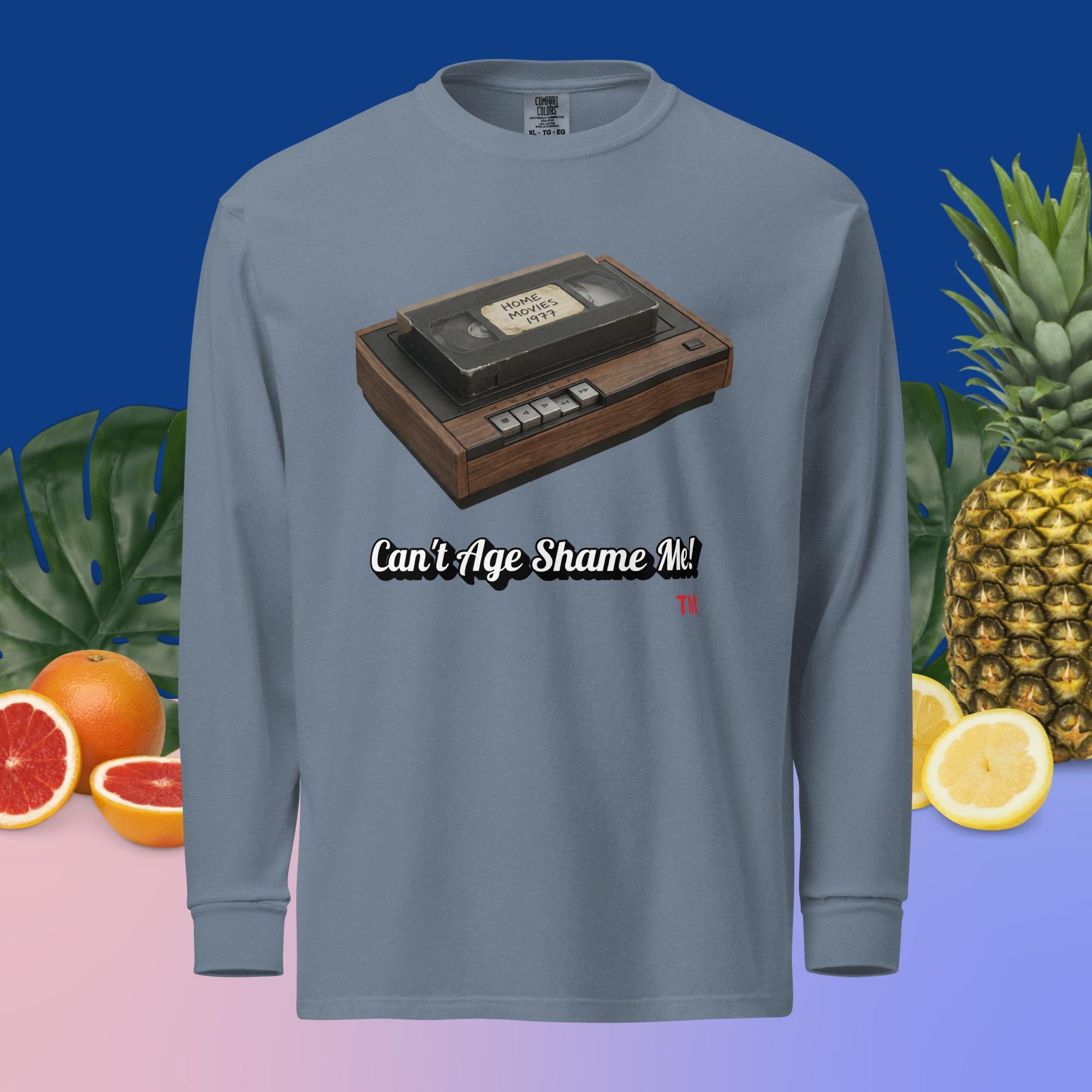 blue jean long-sleeve shirt with a VHS tape design and text 'Can't Age Shame Me!' on a colorful background with fruits and plants.