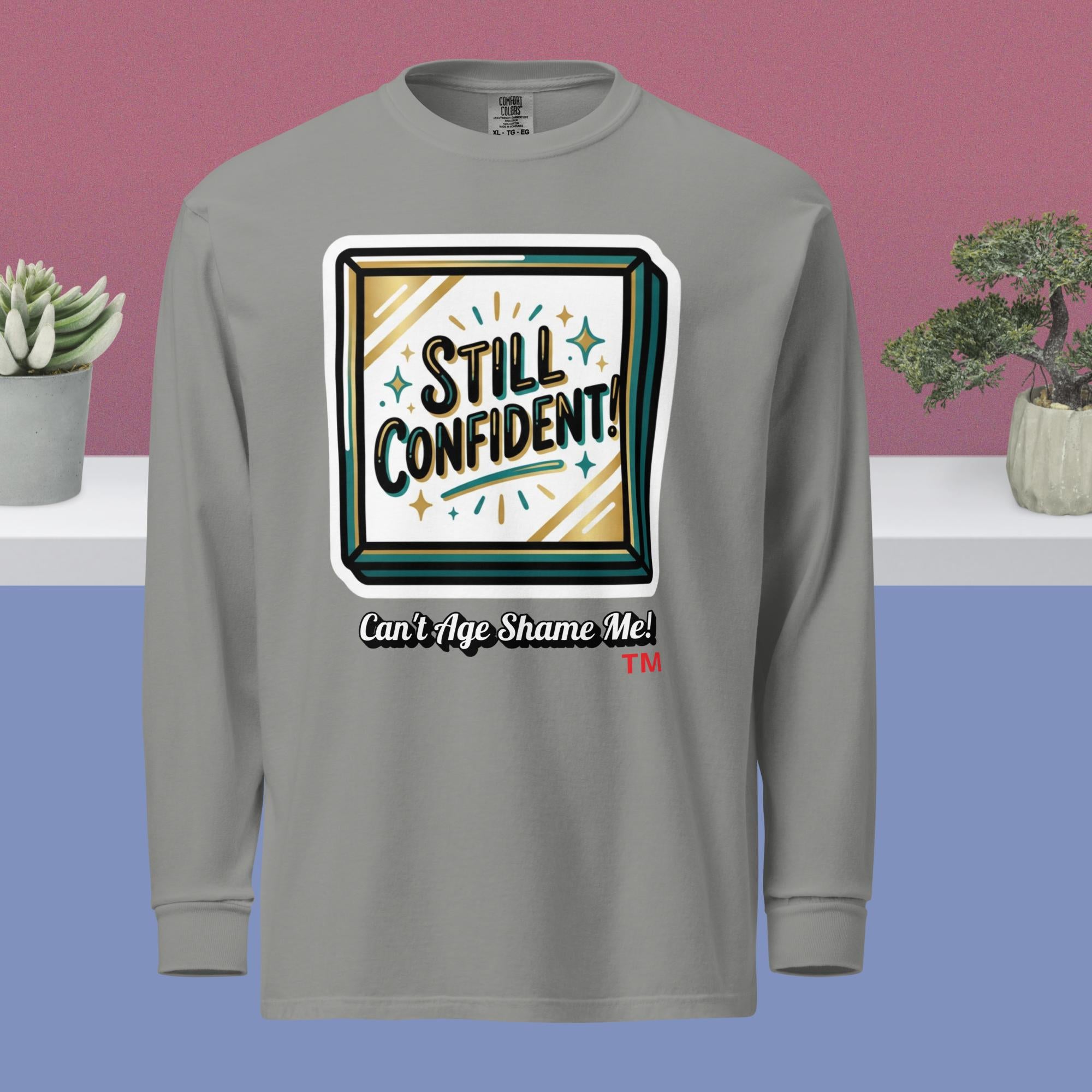 Gray long-sleeve shirt with 'Still Confident! Can't Age Shame Me!' design on a blue and pink gradient background.