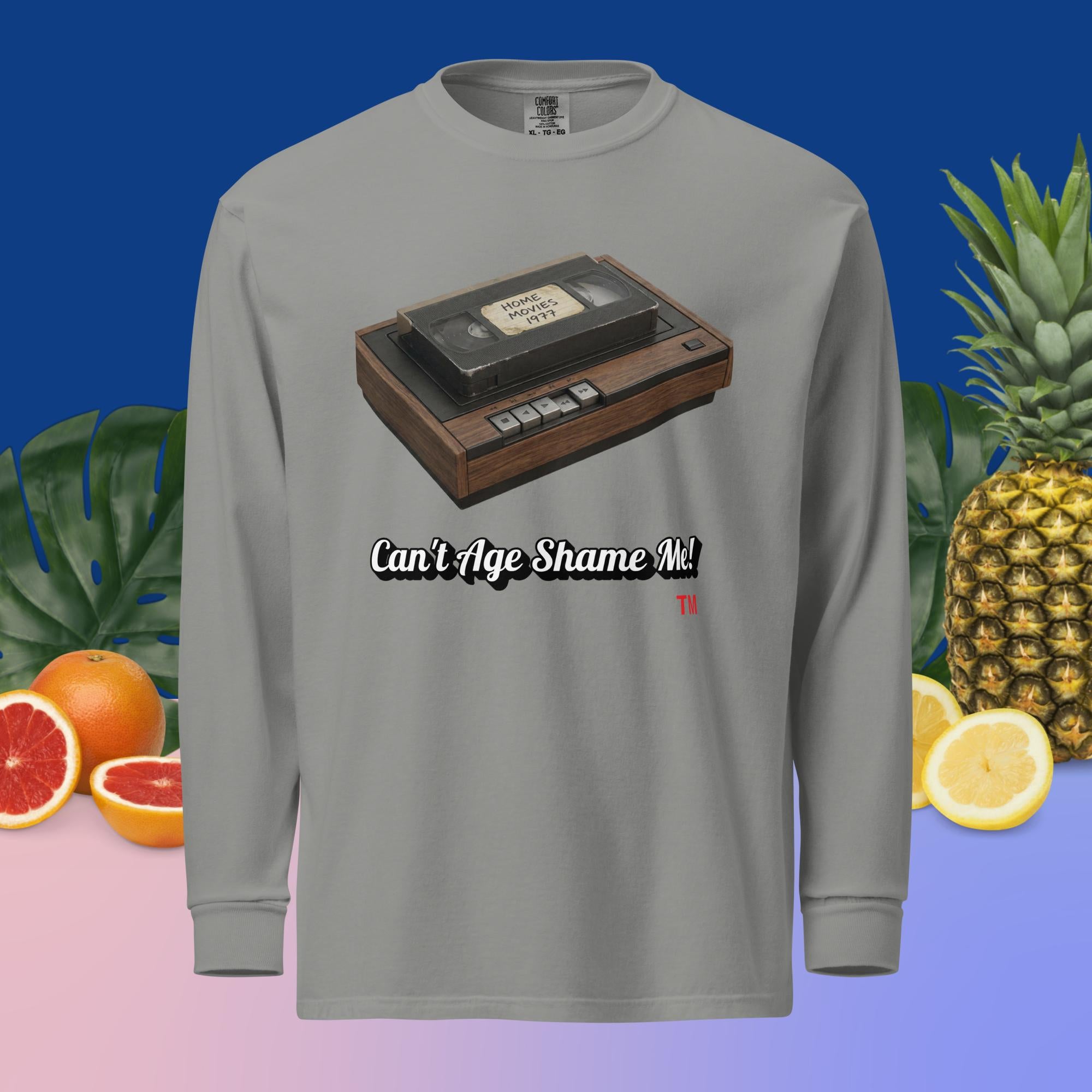 Gray long-sleeve shirt with a cassette tape graphic and text 'Can't Age Shame Me!' on a colorful background with fruits and plants.