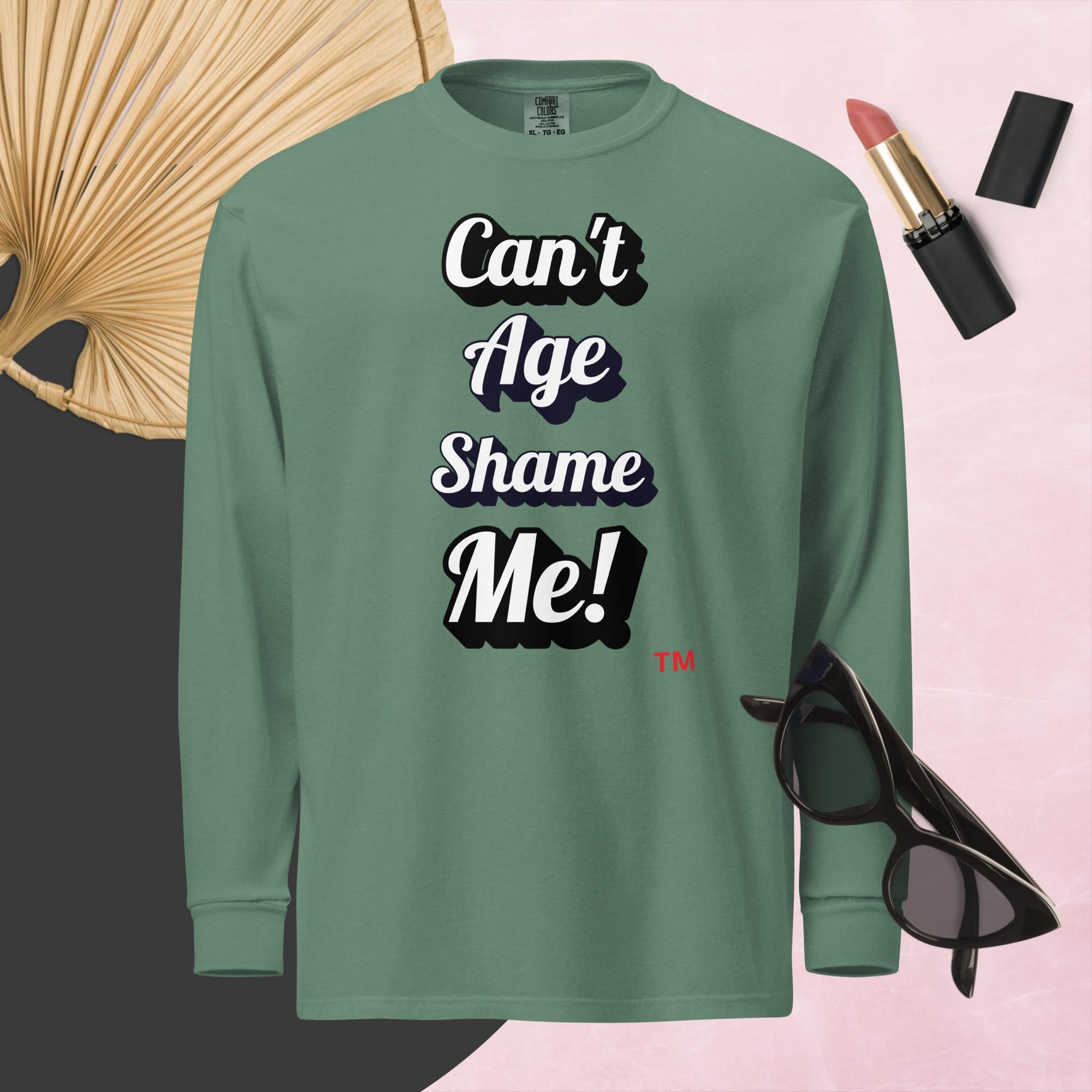 Green long-sleeve shirt with 'Can't Age Shame Me!' text, surrounded by lipstick and sunglasses on a pink background