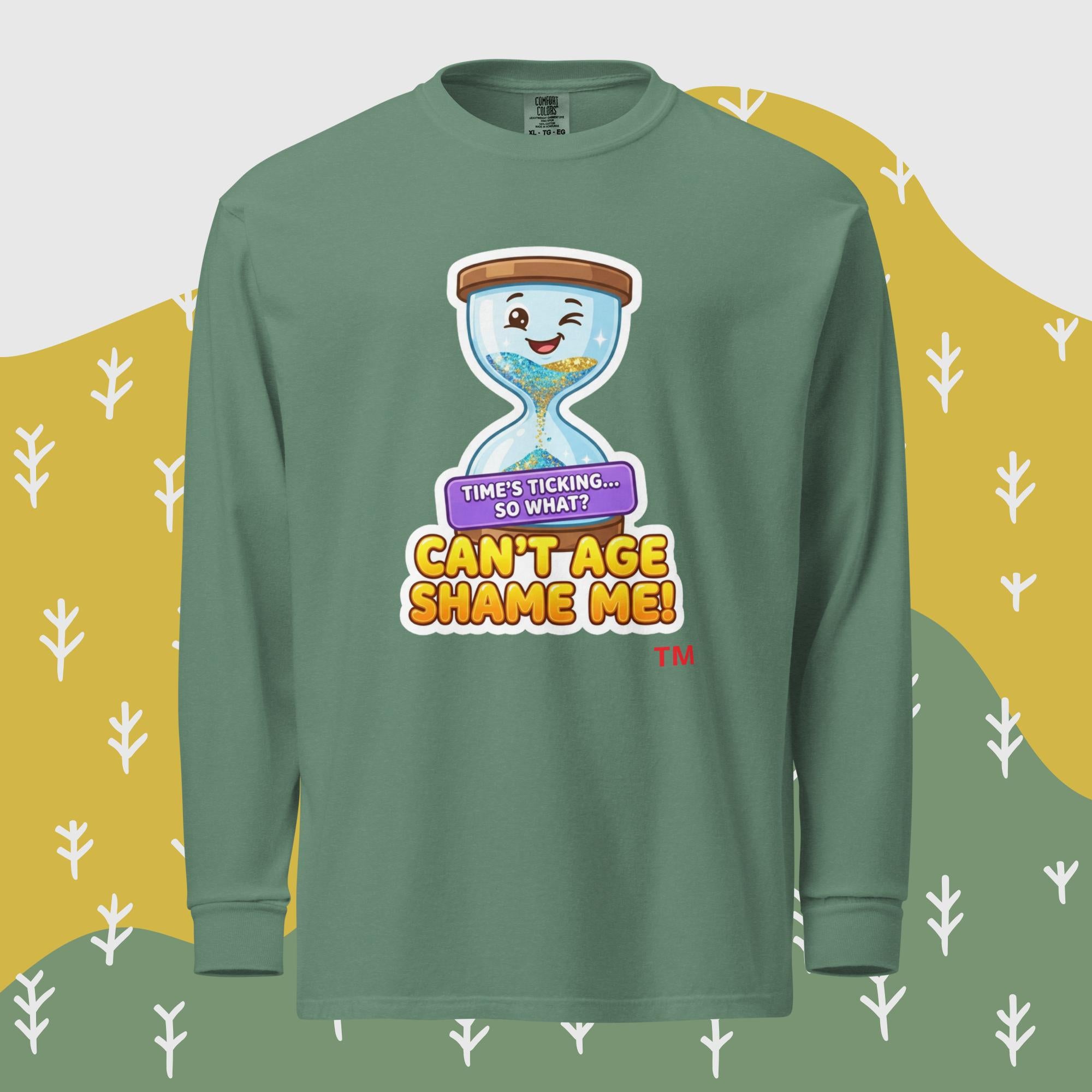 Green long-sleeve shirt with a cartoon hourglass design and text 'Can't Age Shame Me' graphic on a patterned background

