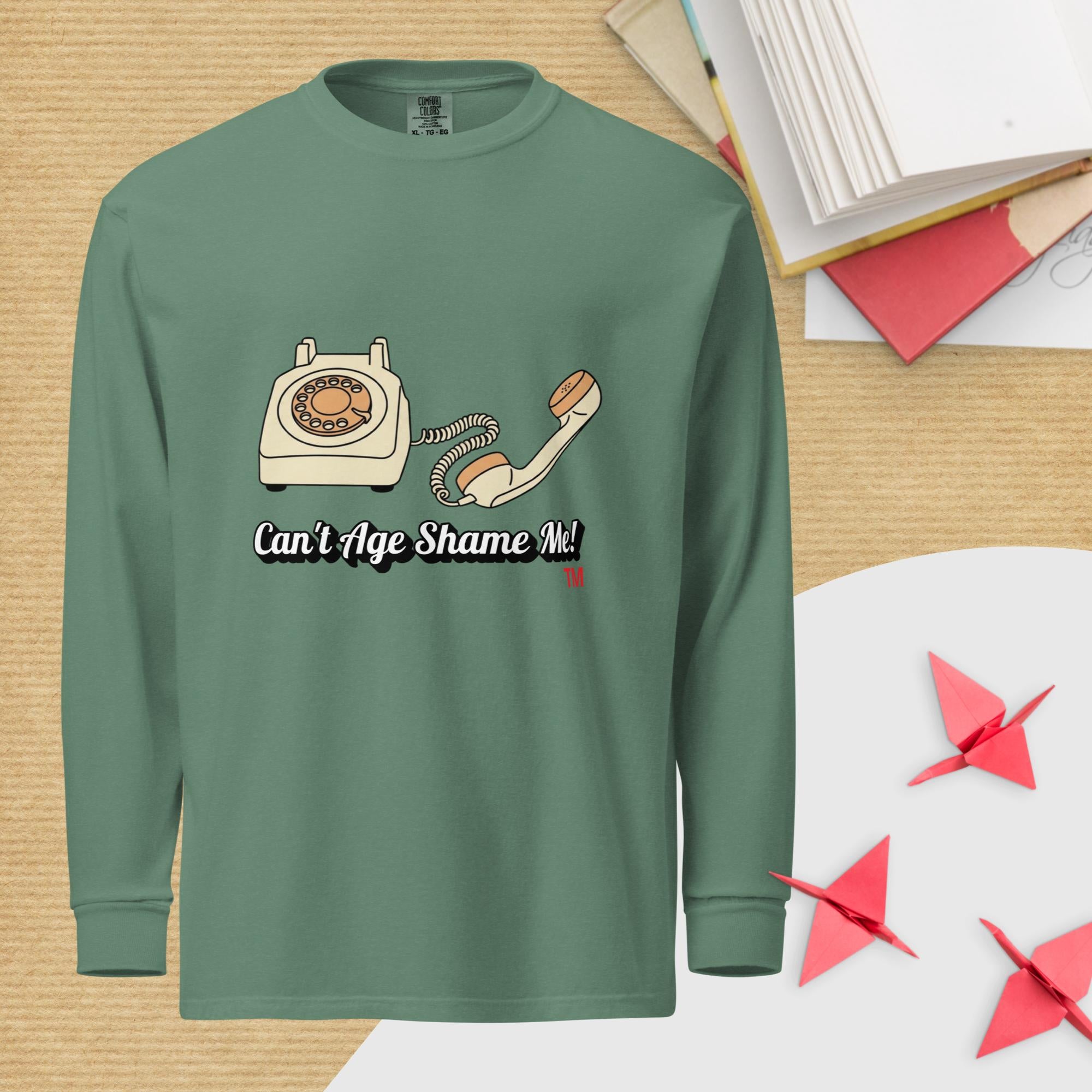 Green long-sleeve shirt with a phone graphic and text 'Can't Age Shame Me!' on a wooden surface.