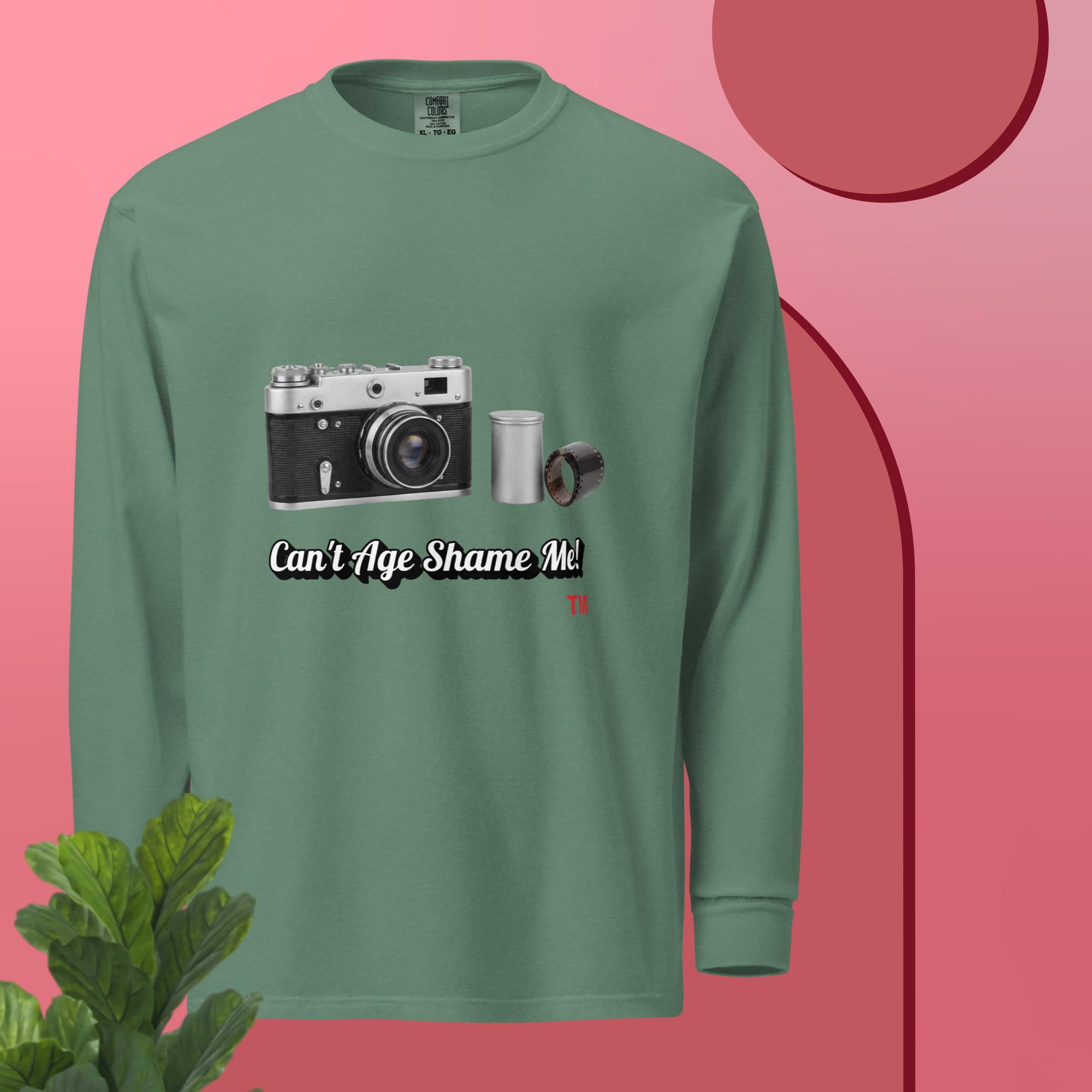 Green long-sleeve shirt with camera graphic and text 'Can't Age Shame Me' on a pink background