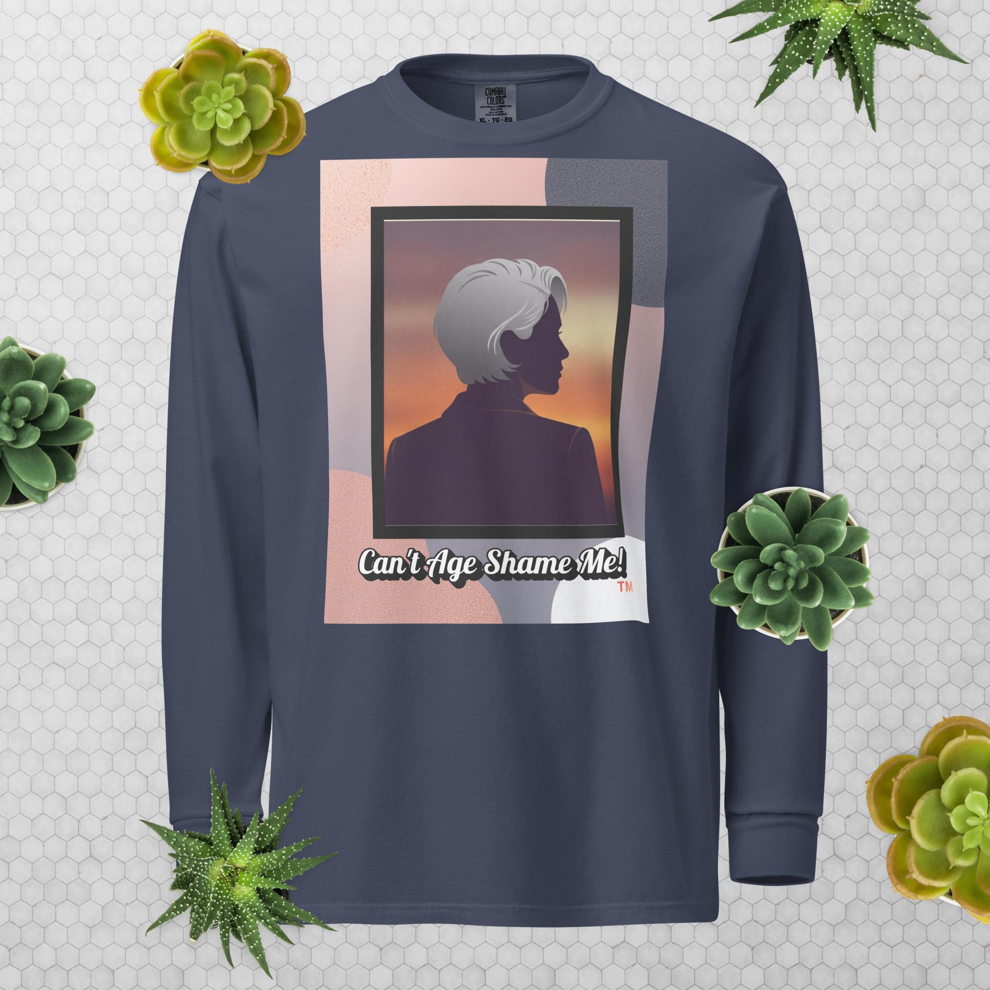 Navy Blue long-sleeve shirt with a graphic design featuring a woman with gray hair silhouette and text: Can’t Age Shame Me! surrounded by decorative plants on a light gray background.

