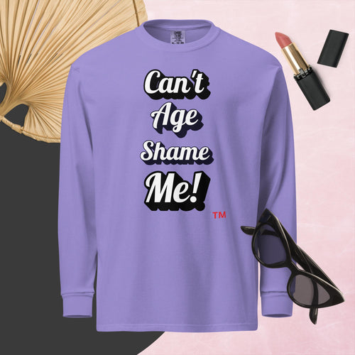 Purple long-sleeve shirt with 'Can't Age Shame Me!' text, surrounded by sunglasses, lipstick, and a decorative leaf on a pink background.