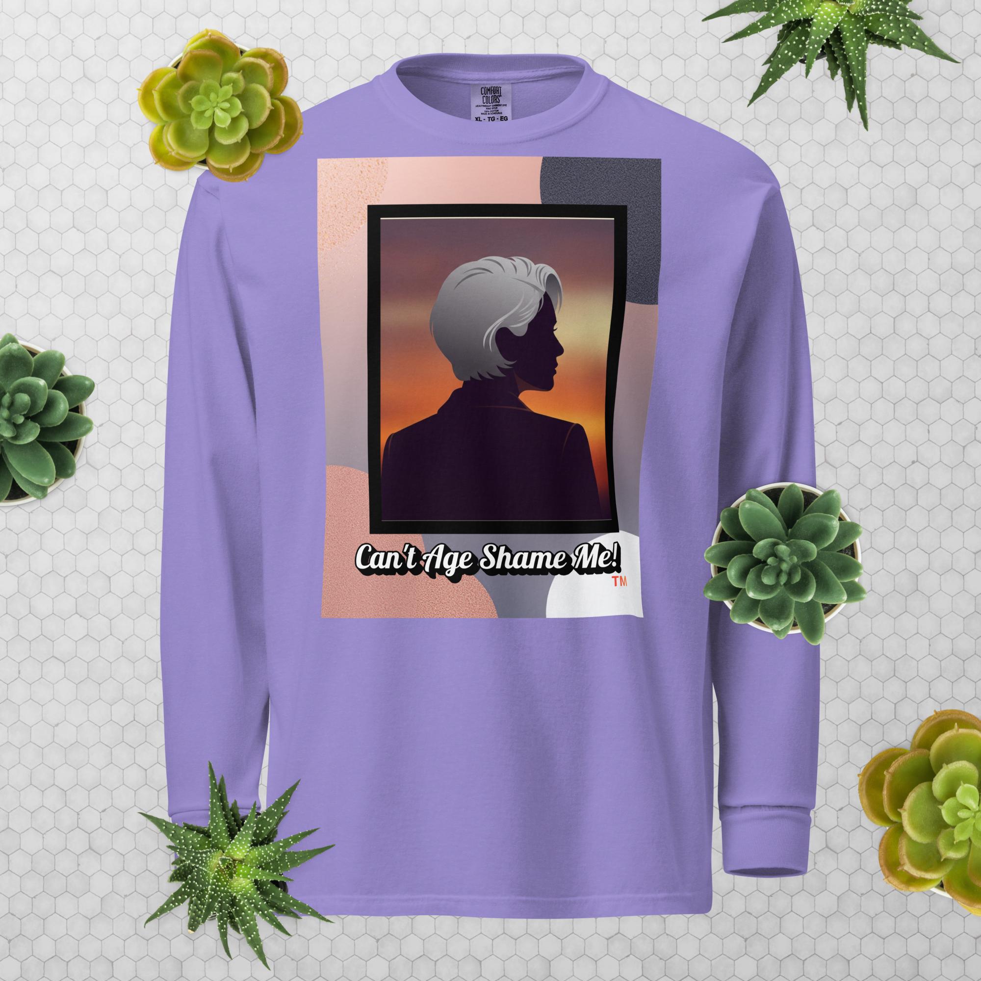 Violet long-sleeve shirt with a graphic design featuring a woman with gray hair silhouette and text: Can’t Age Shame Me! surrounded by decorative plants on a light gray background.

