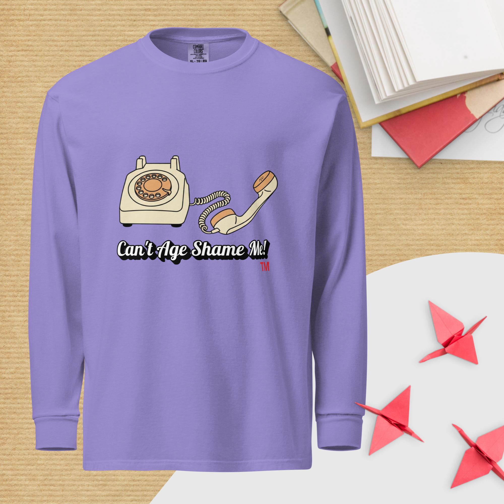 violet  long-sleeve shirt with a graphic of an old telephone and text 'Can't Age Shame Me!' on a wooden surface.