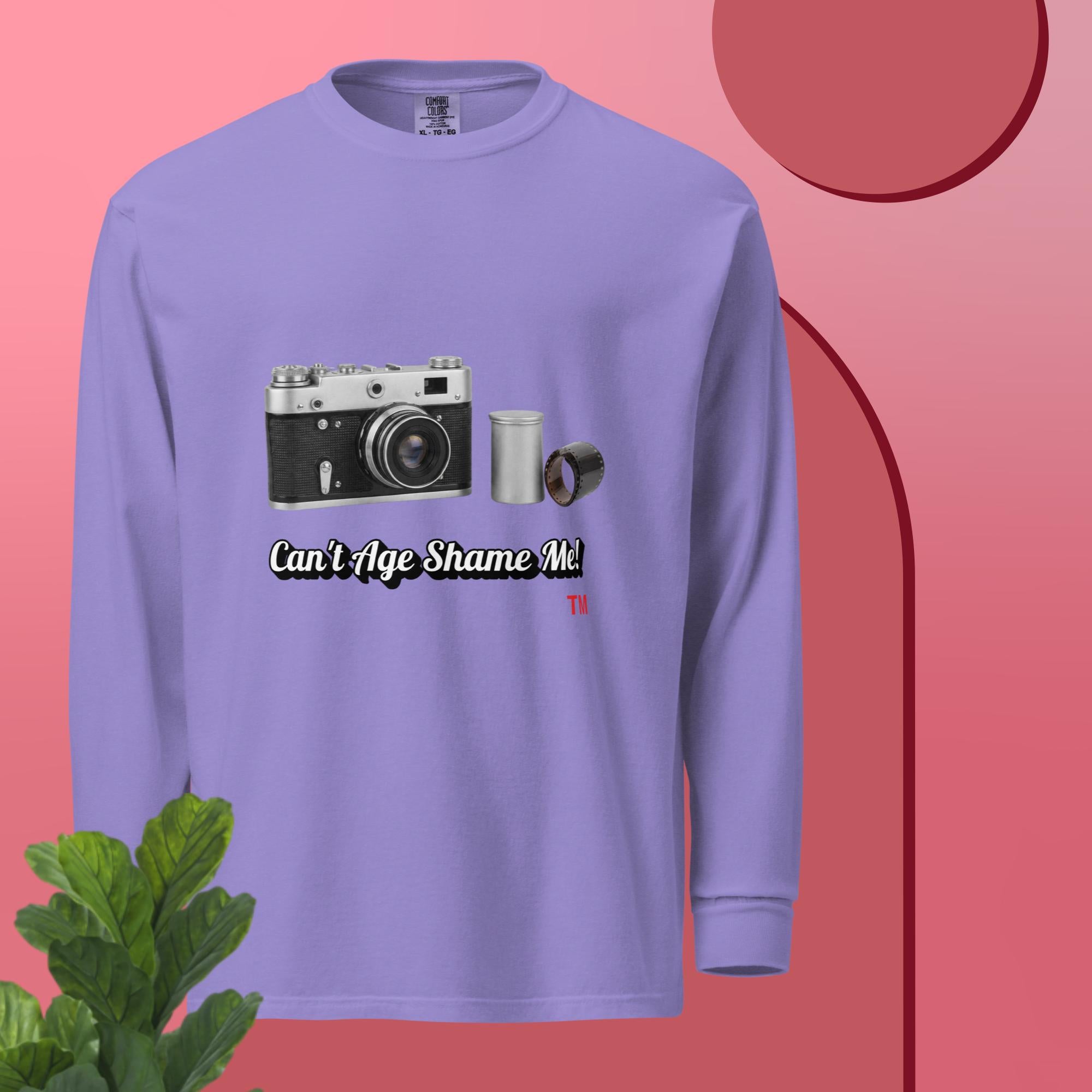 violet long sleeve shirt with camera graphic and text  can't age shame me on a pink background