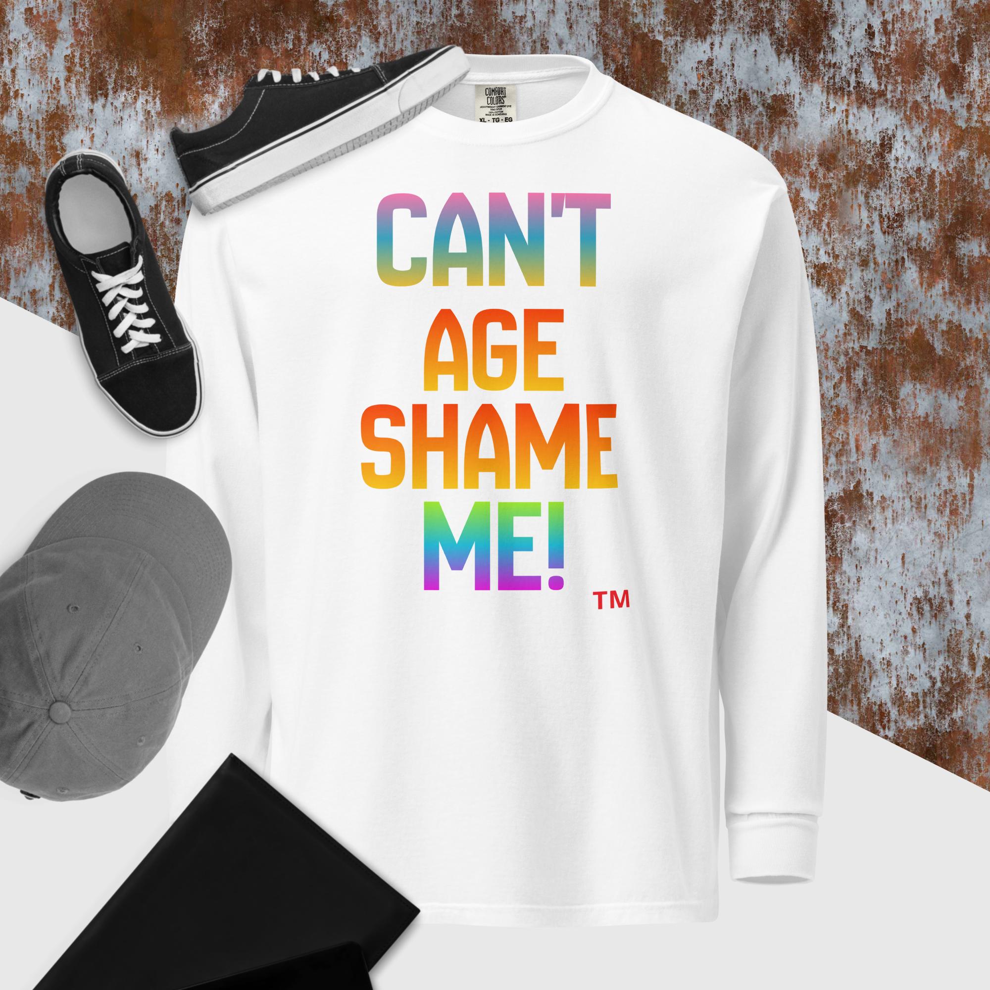 White sweatshirt with colorful text 'CAN'T AGE SHAME ME!' on a textured surface with sneakers and a cap.