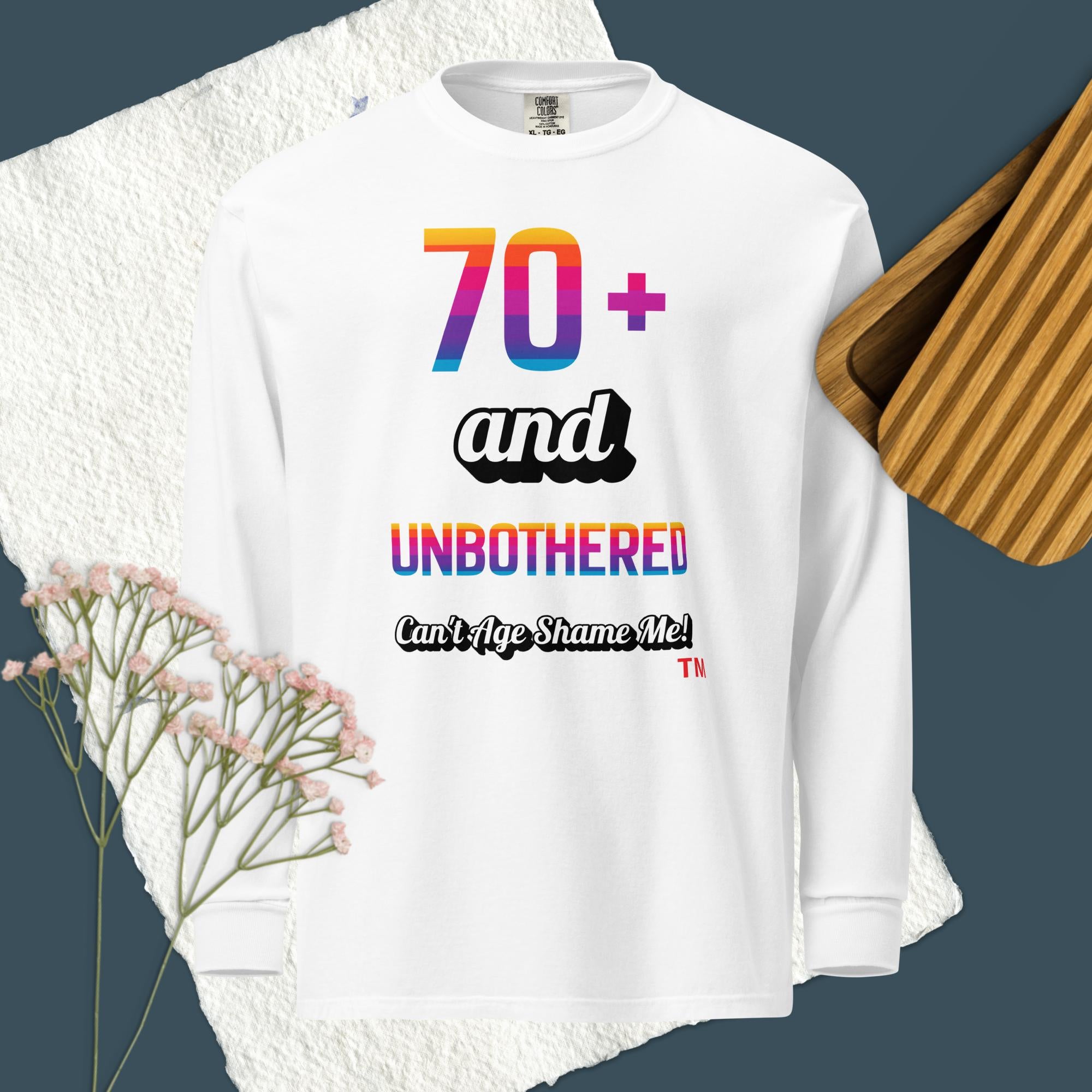 White long-sleeve shirt with colorful text design on a textured surface with flowers and wooden object.