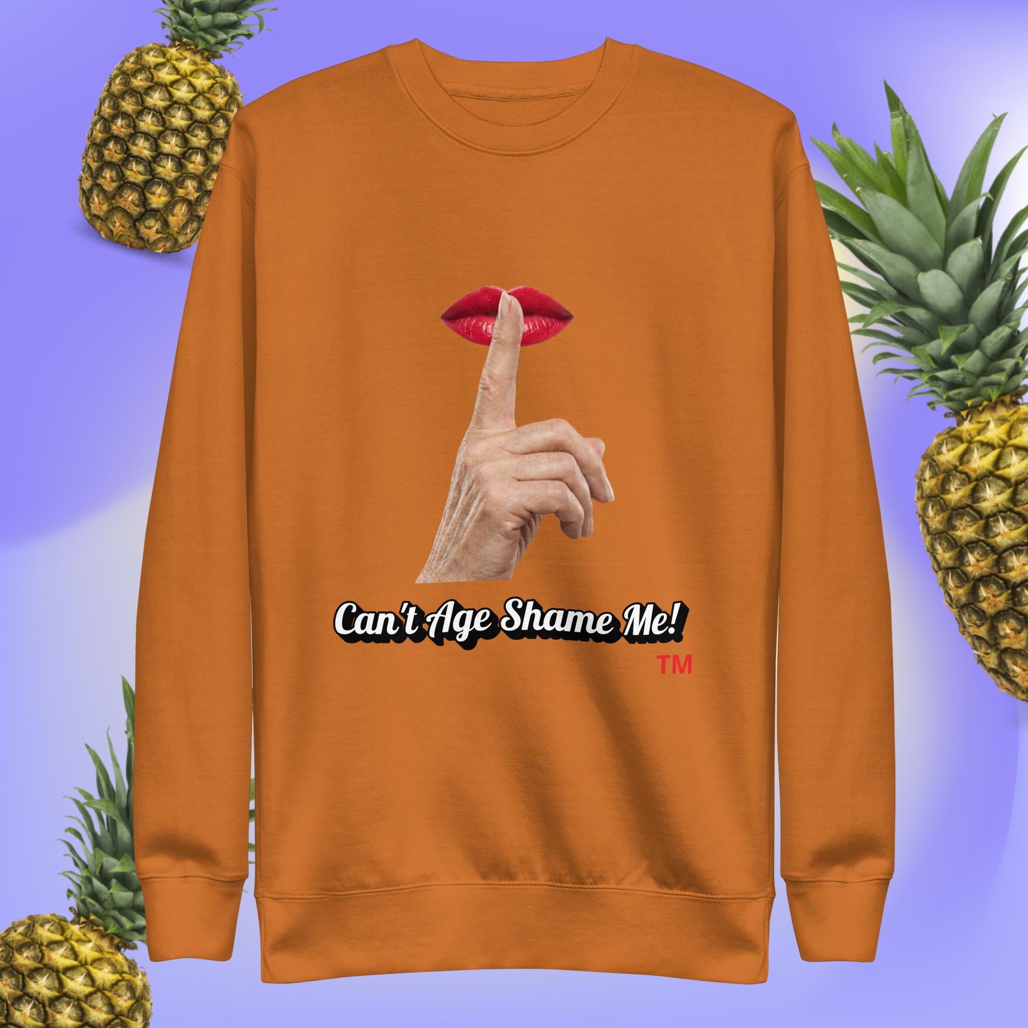 Adobe sweatshirt with a graphic design of finger on mouth and text 'Can't Age Shame Me!' on a blue background with pineapples.