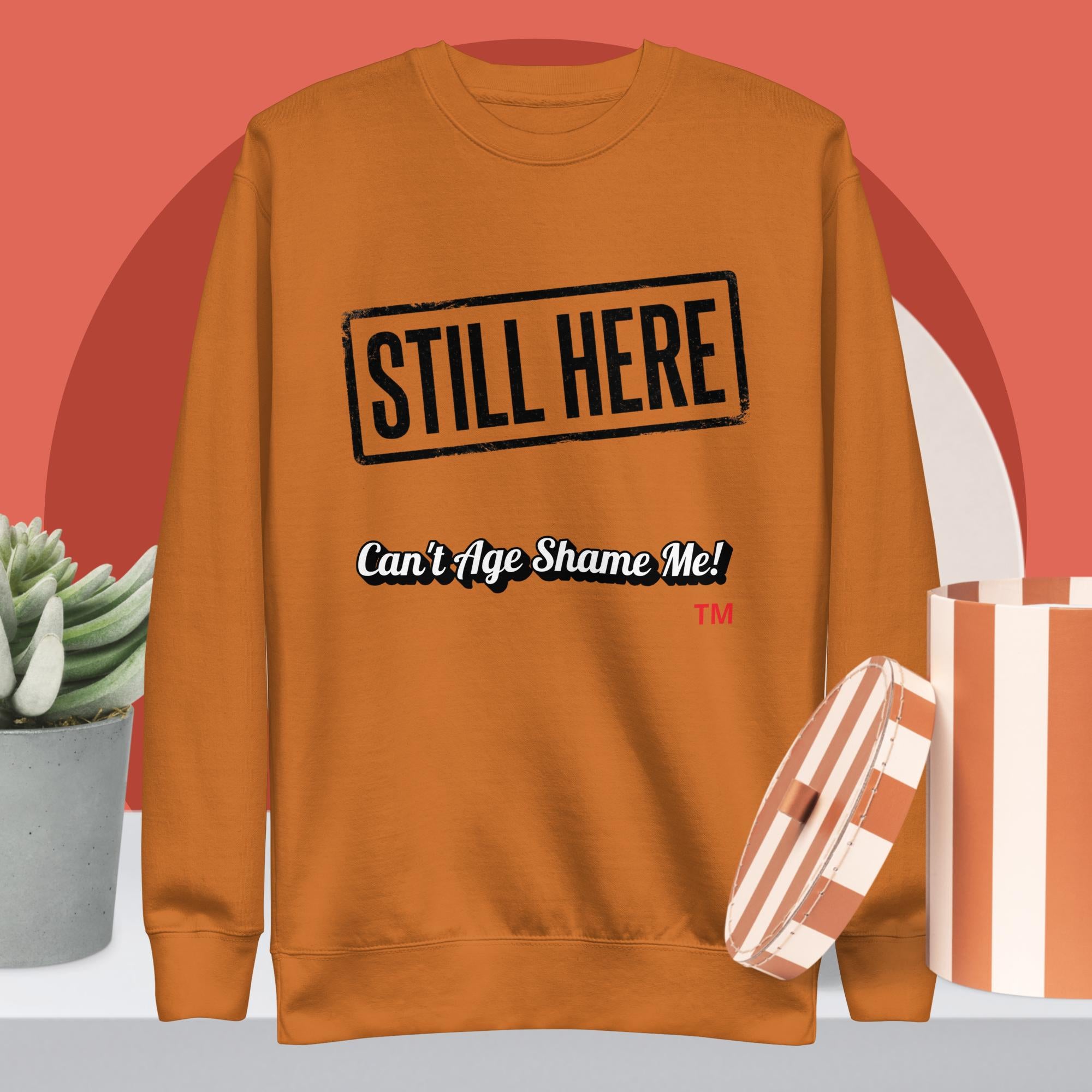 Adobe sweatshirt with 'STILL HERE Can't Age Shame Me!' text on a red background