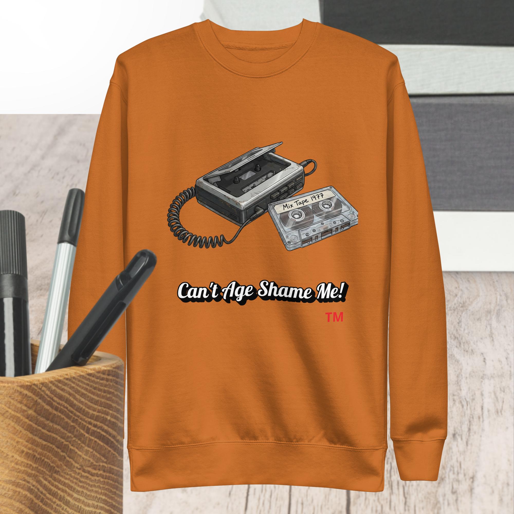 adobe  sweatshirt with cassette tape design and text 'Can't Age Shame Me!' on a wooden surface.