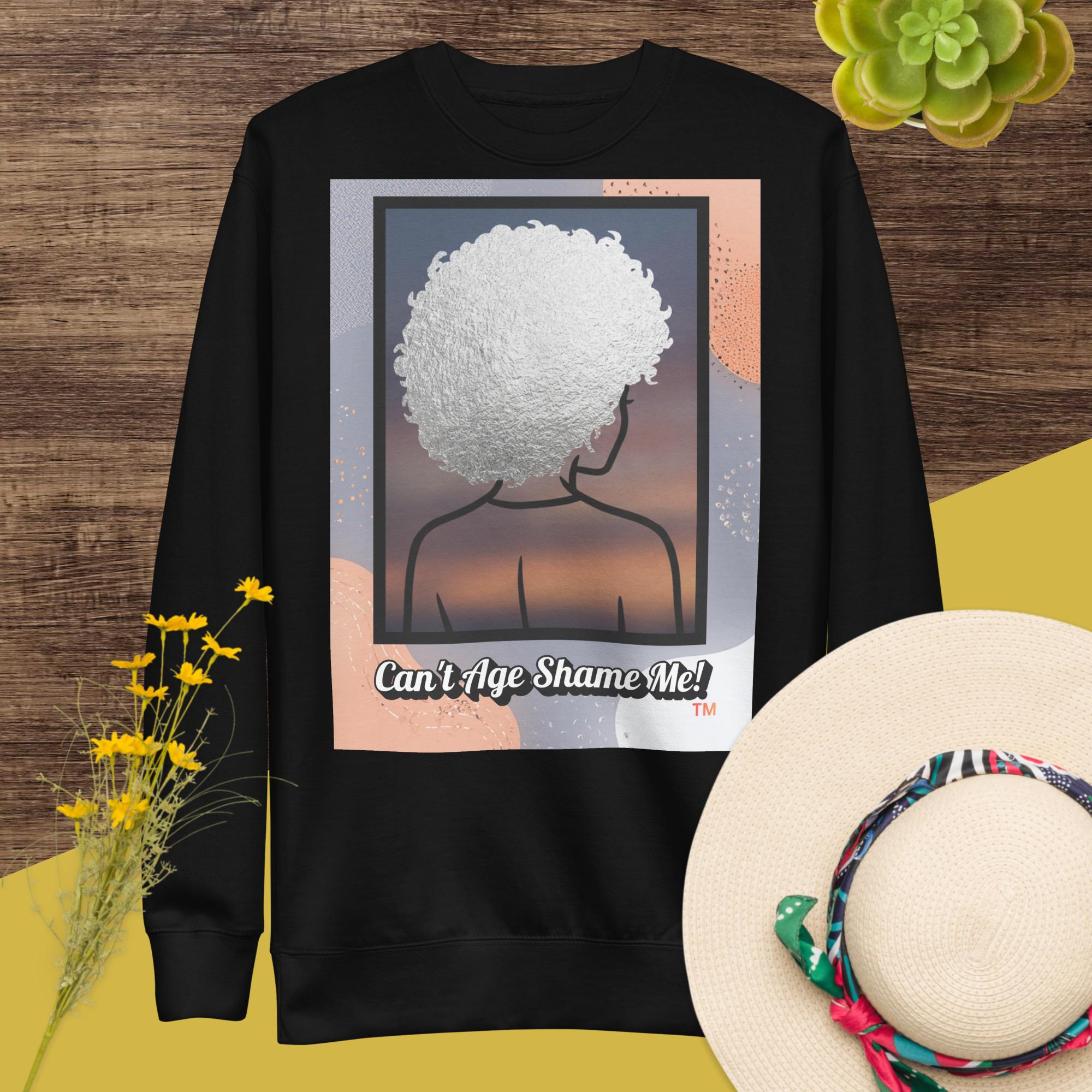 Black sweatshirt with a graphic design of a person with textured hair and text 'Can't Age Shame Me!' on a colorful background.