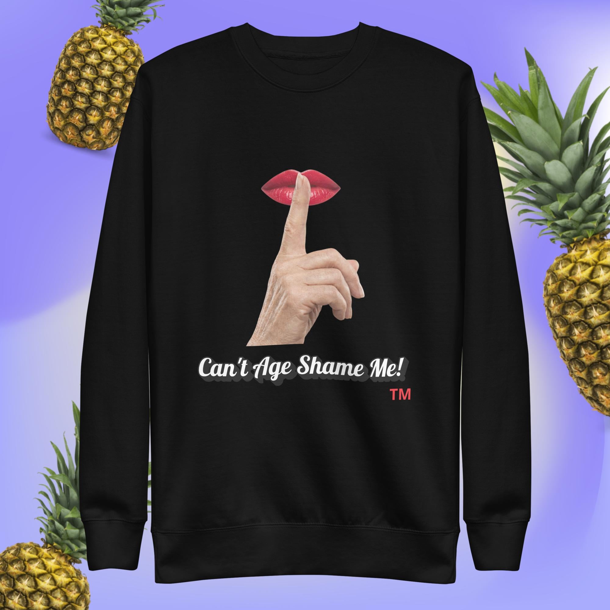 Black sweatshirt with a graphic design of finger on mouth and text 'Can't Age Shame Me!' on a blue background with pineapples.