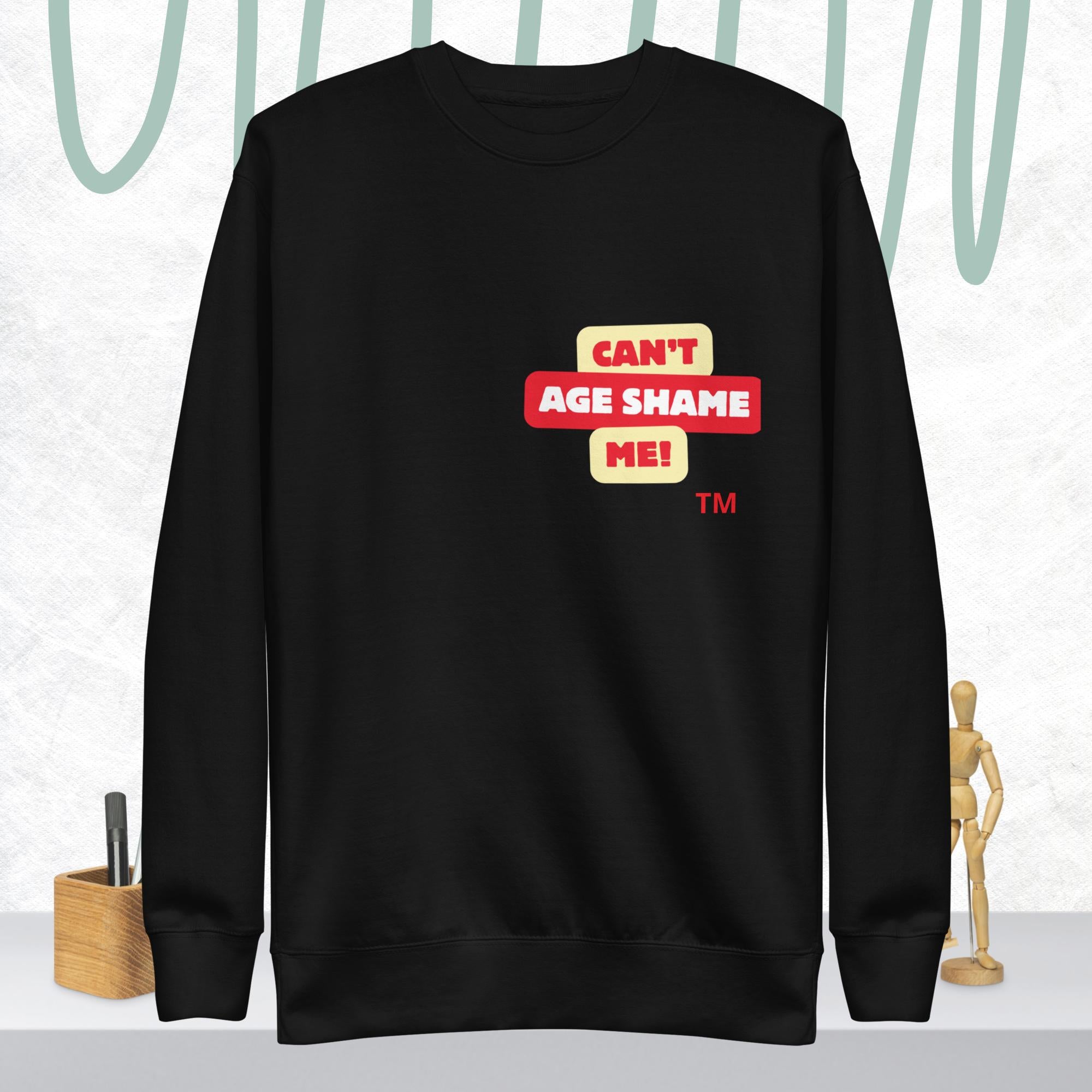 Black sweatshirt with 'CAN'T AGE SHAME ME!' text logo on a light gray background