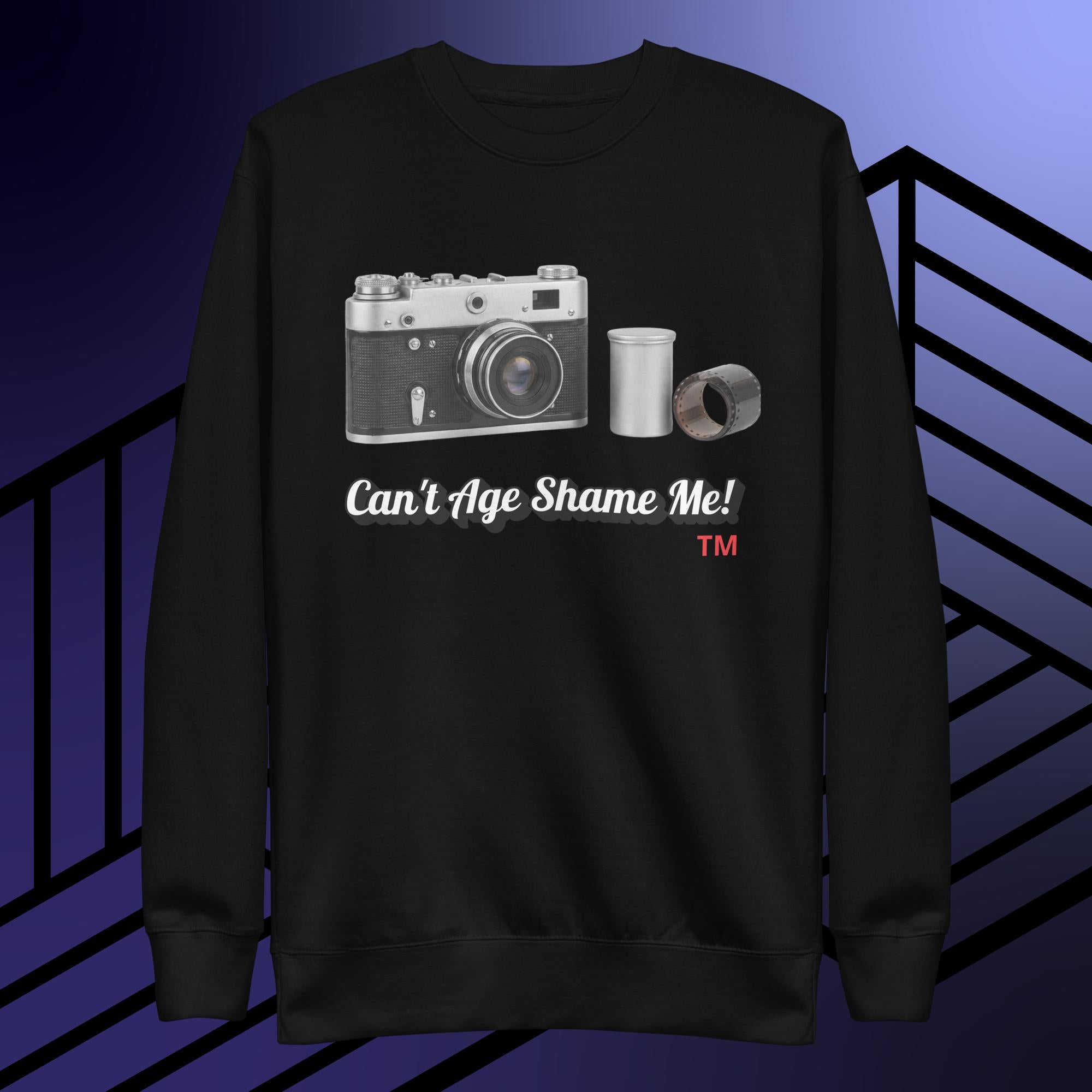 Black sweatshirt with camera graphic and text can't age shame me! on a blue and black striped background.