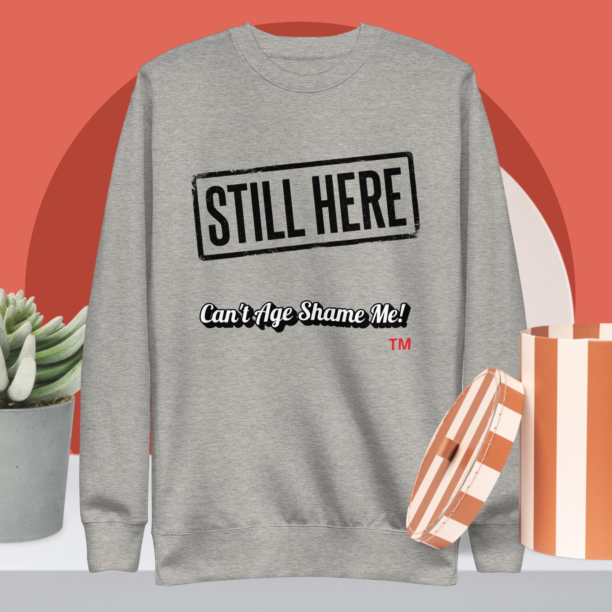 Gray sweatshirt with 'STILL HERE Can't Age Shame Me!' text on a red and white background