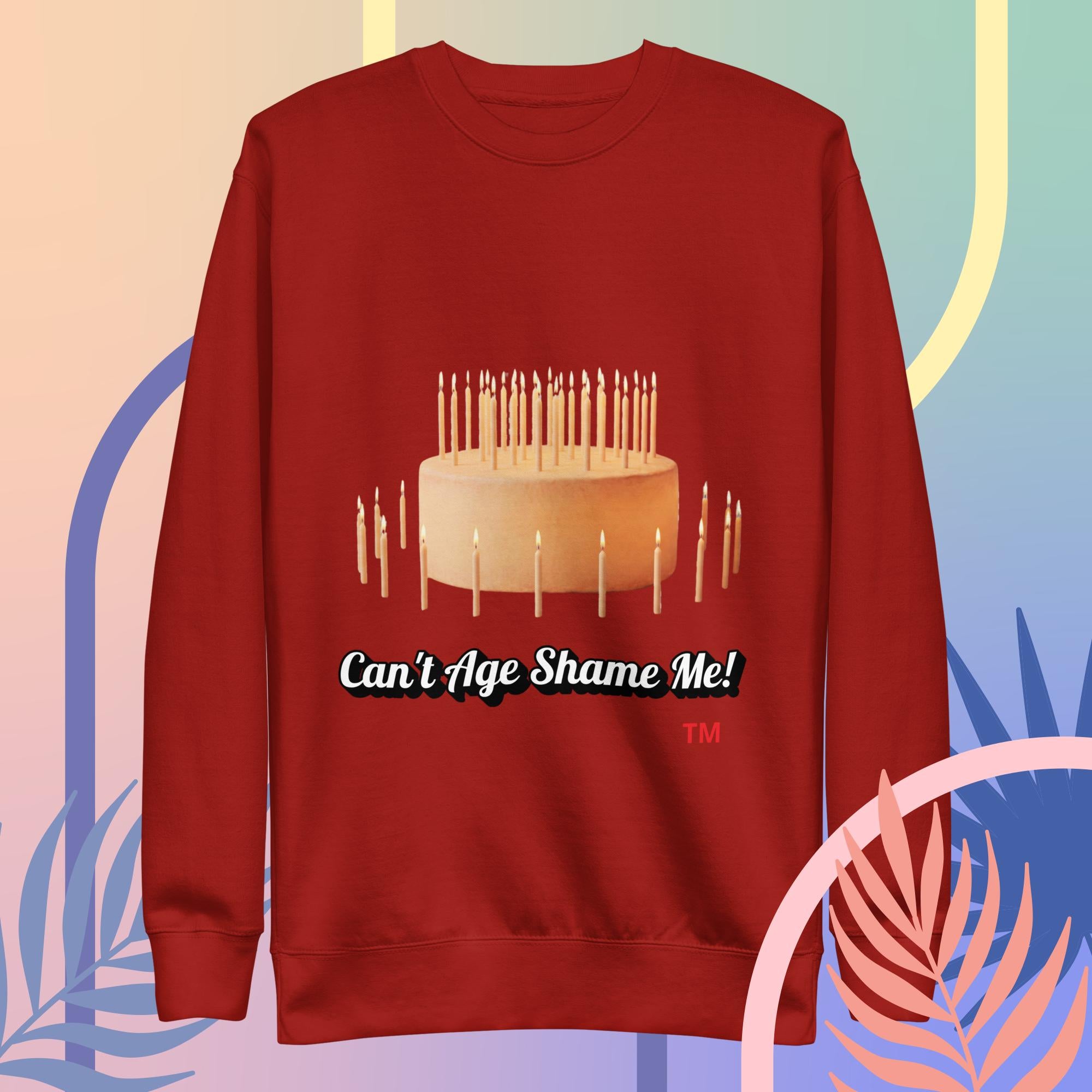 Red sweatshirt with a cake and candles design and text 'Can't Age Shame Me!' on a colorful background.