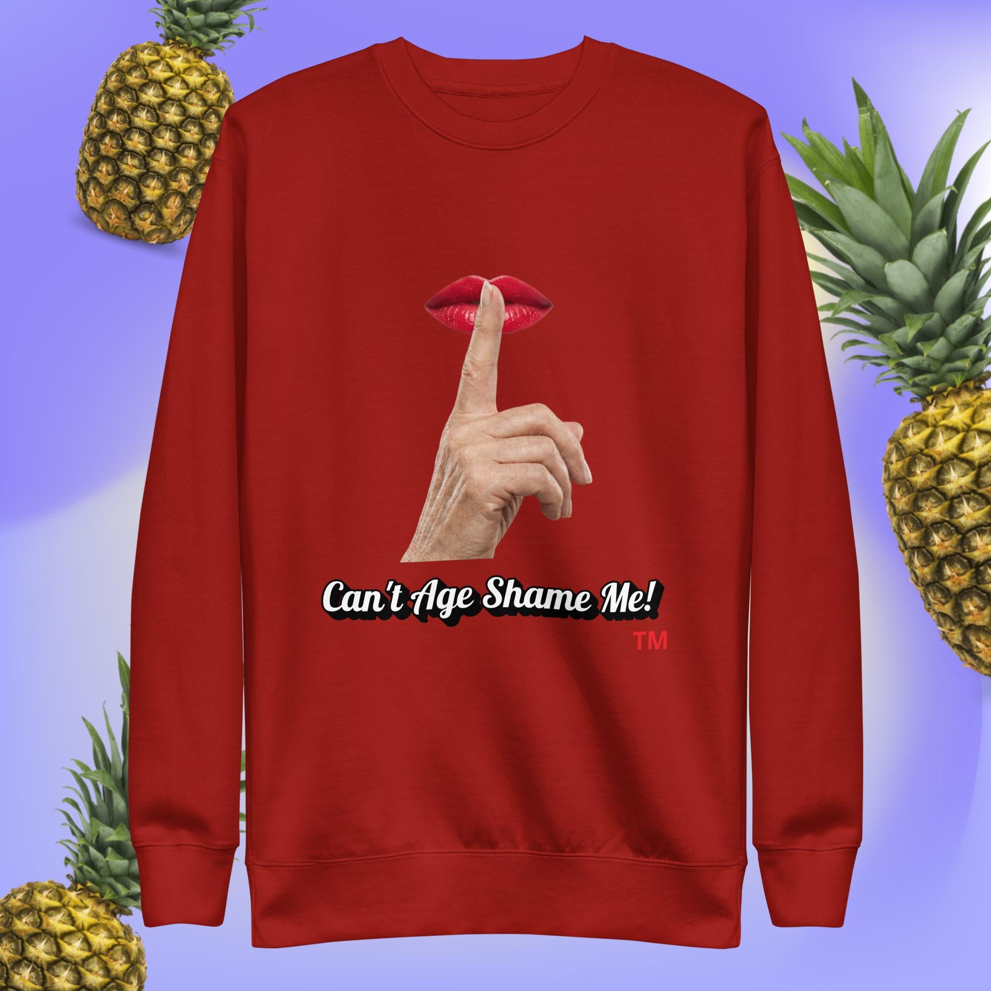 Cardinal sweatshirt with a graphic design of finger on mouth and text 'Can't Age Shame Me!' on a blue background with pineapples.