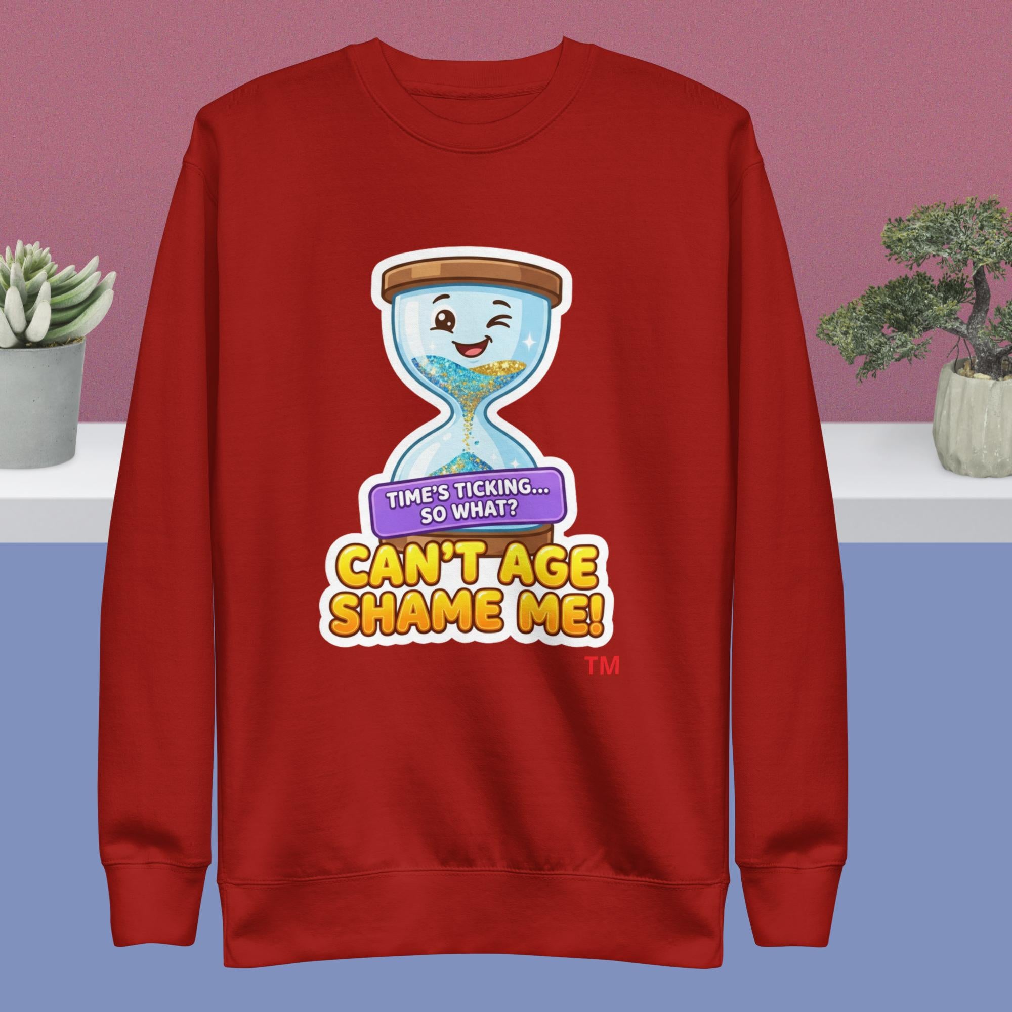 Red sweatshirt with a cartoon hourglass design and humorous text on a pink and blue gradient background.