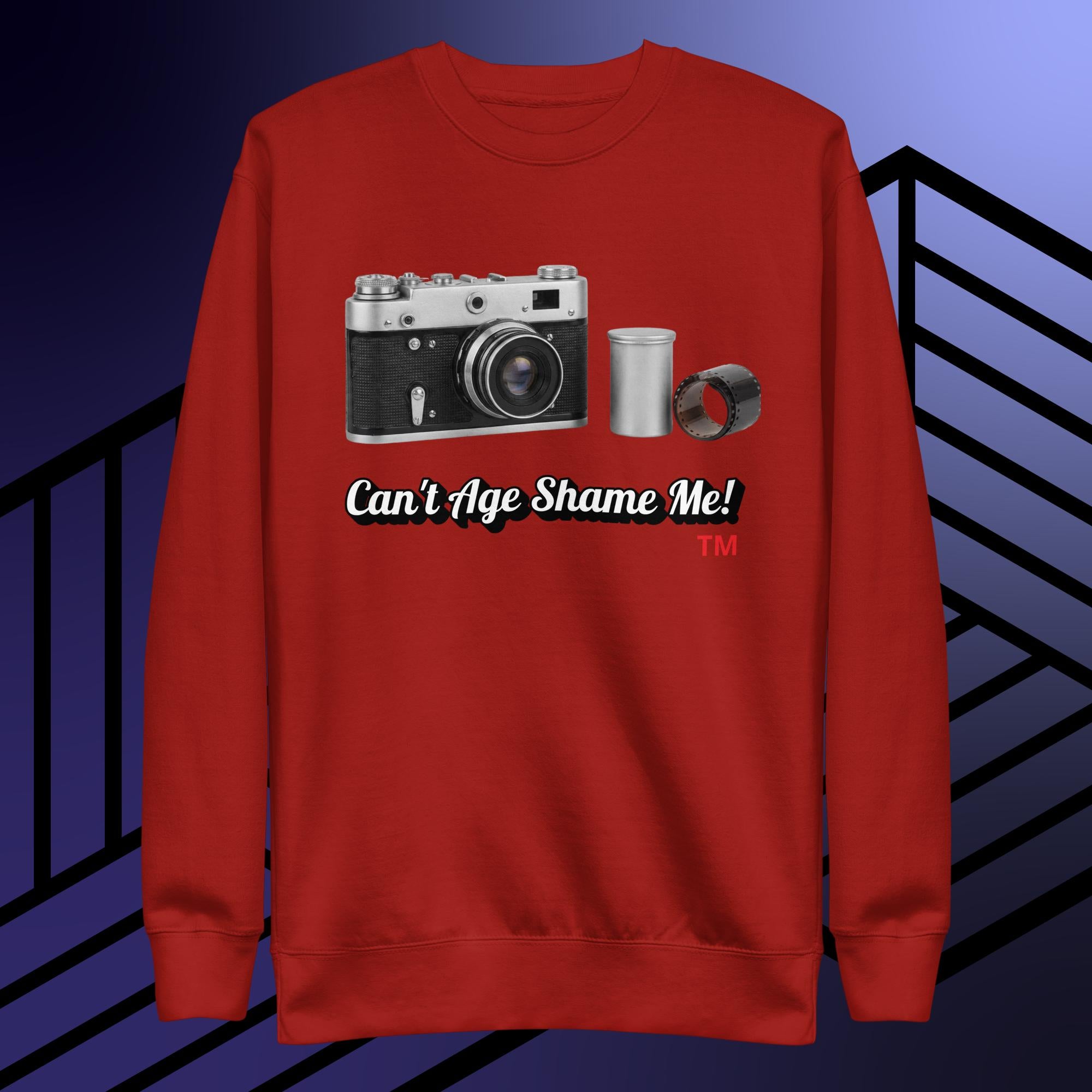 Red sweatshirt with camera graphic and text 'Can't Age Shame Me!' on a blue and black striped background
