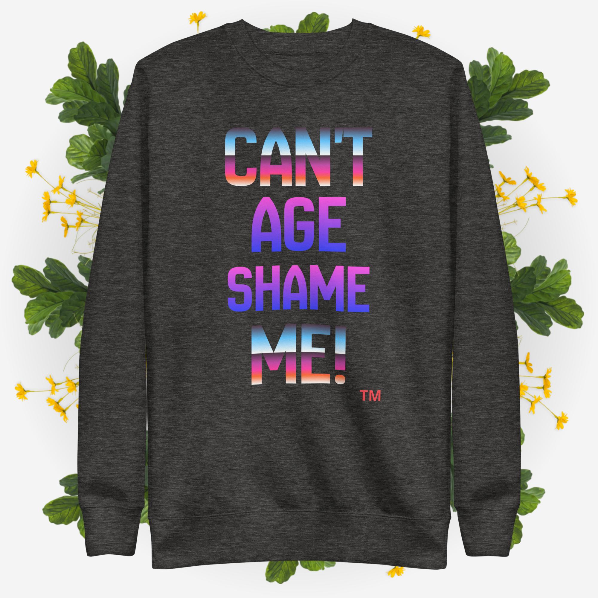 Dark gray sweatshirt with colorful text 'CAN'T AGE SHAME ME!' on a light background with green leaves and yellow flowers.