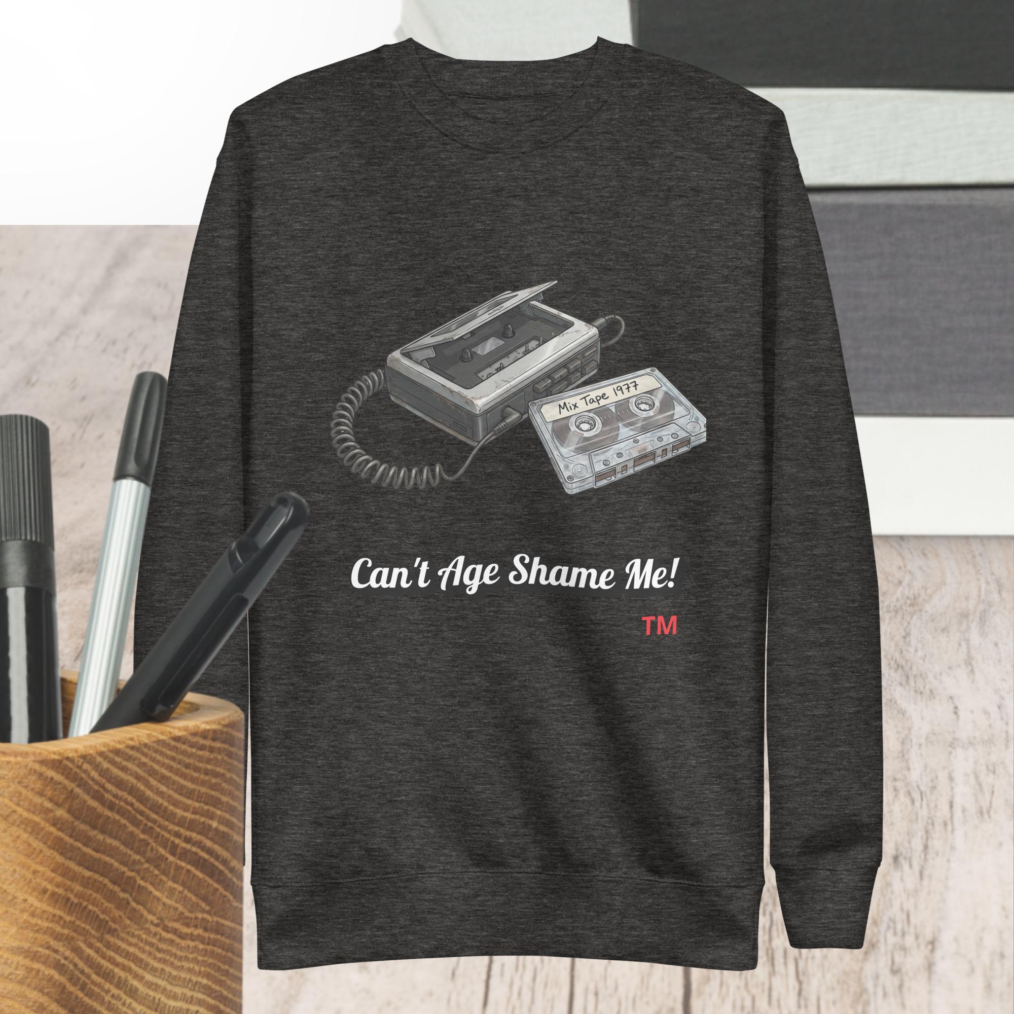 Dark gray sweatshirt with cassette tape design and text 'Can't Age Shame Me!' on a wooden surface.