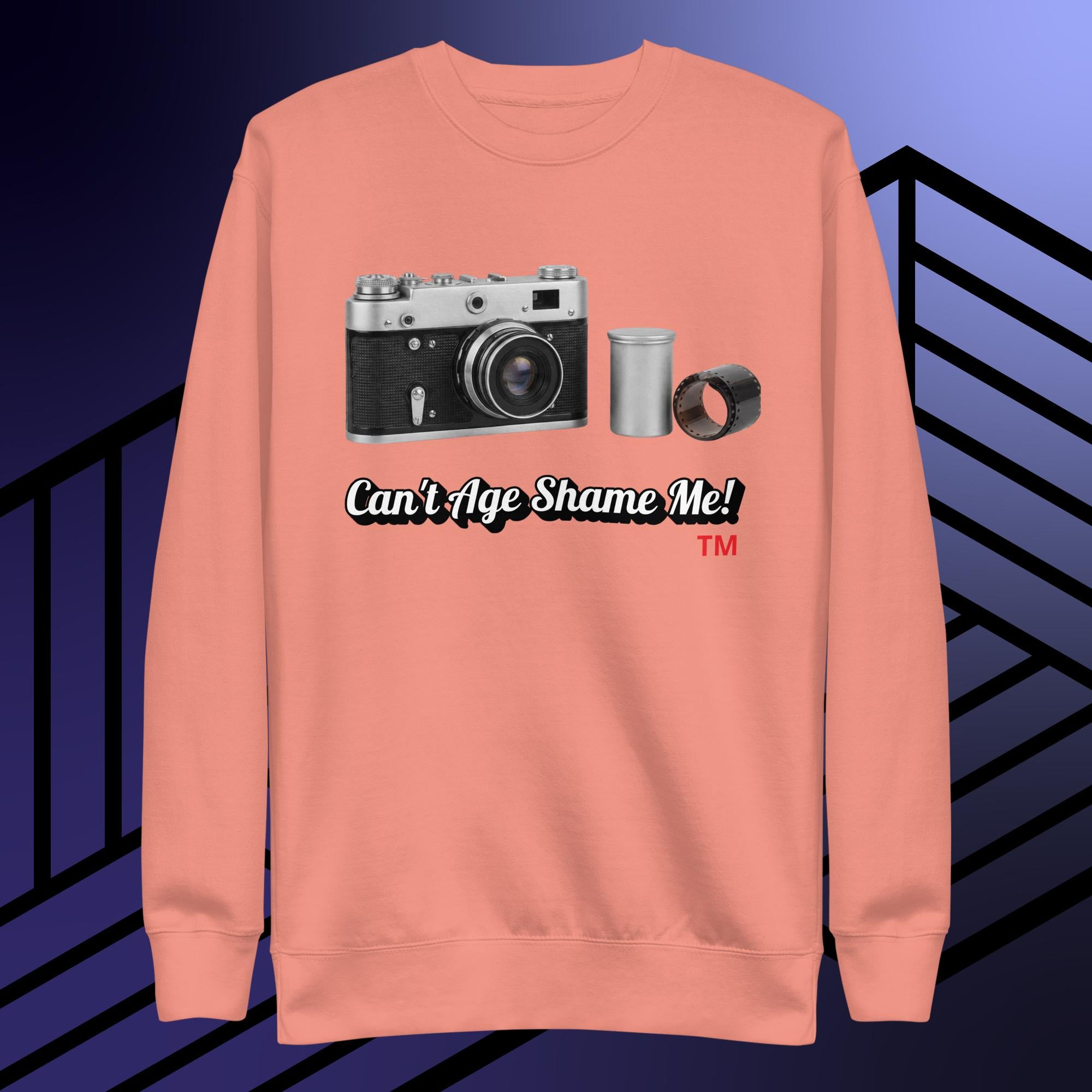 dusty rose sweatshirt with camera graphic and text can't age shame me! on a blue and black striped background.